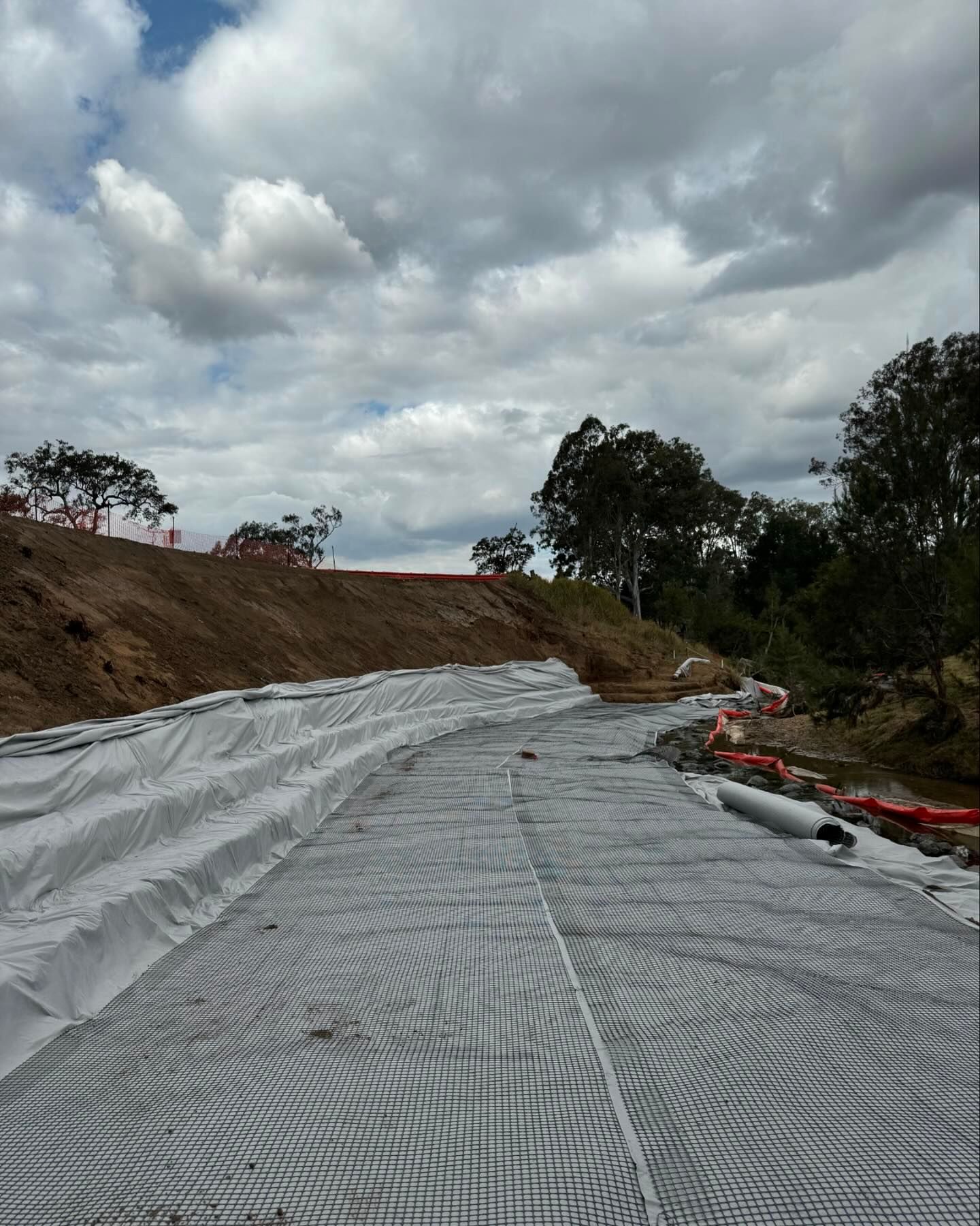 Geotextile matting has been installed along the surface and edge of a river bank. 