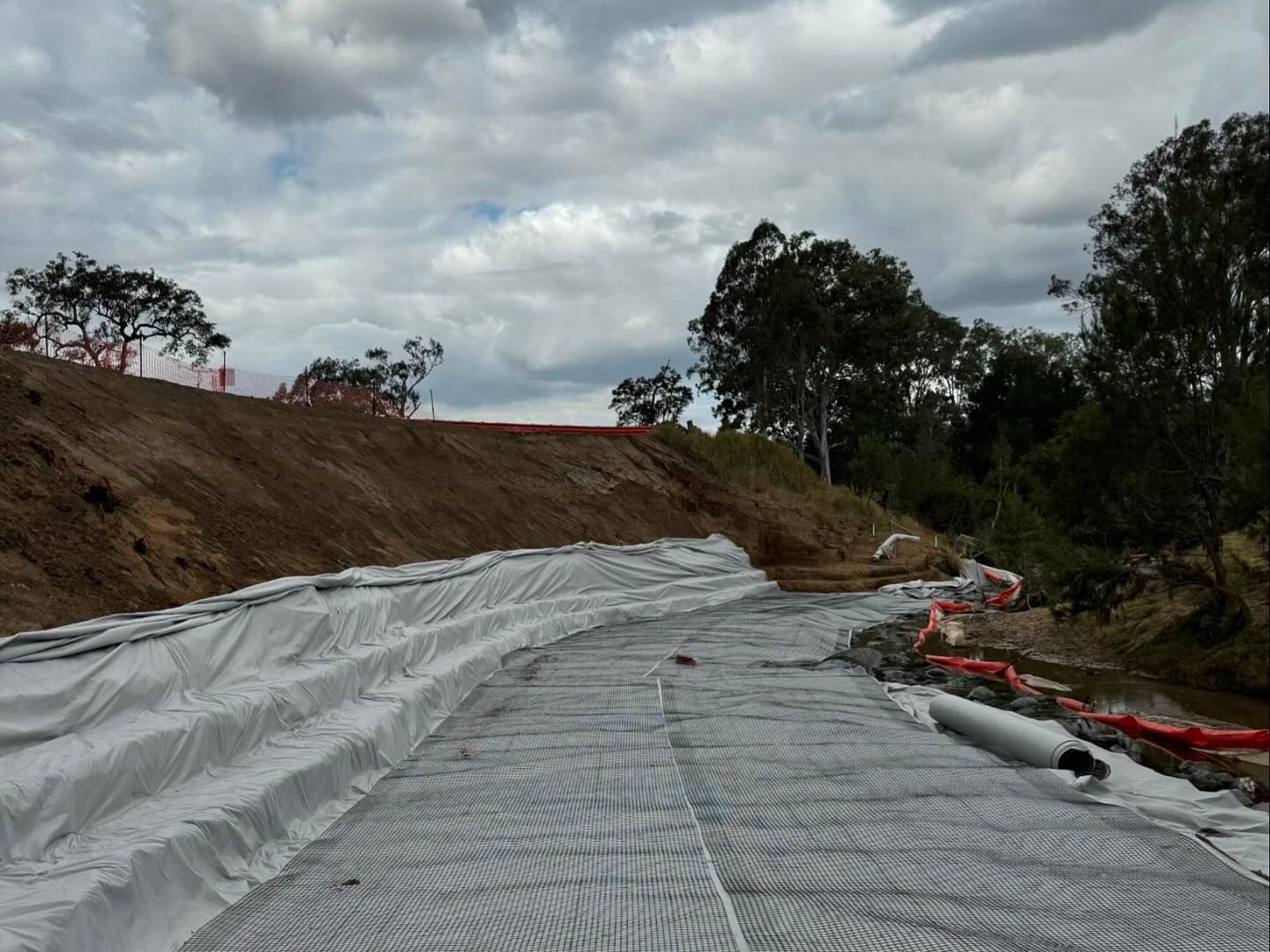 Geotextile matting has been installed along the surface and edge of a river bank.