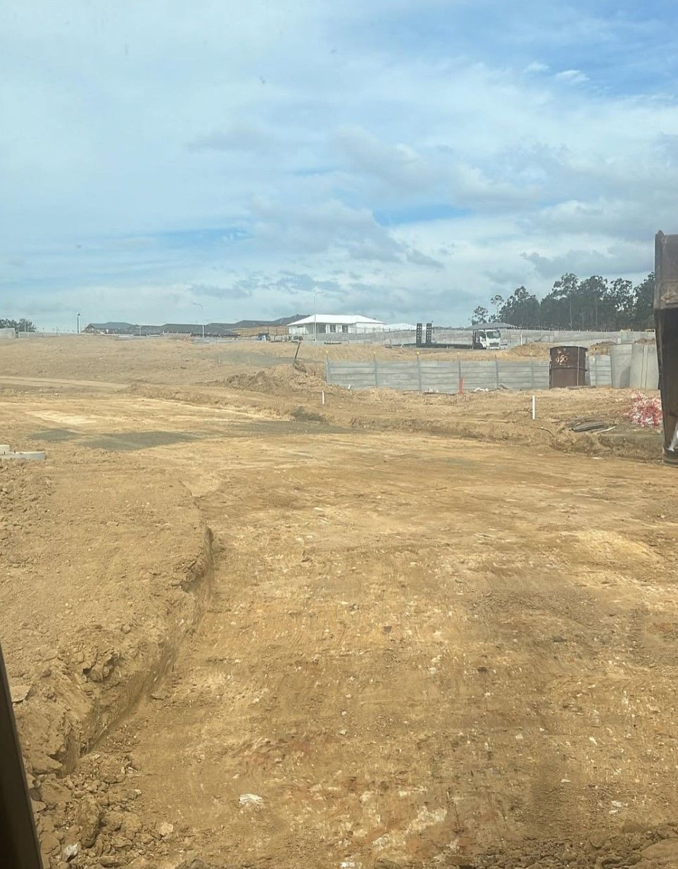 A large levelled dirt pad with a fence in the background. Ready for the next phase of construction.
