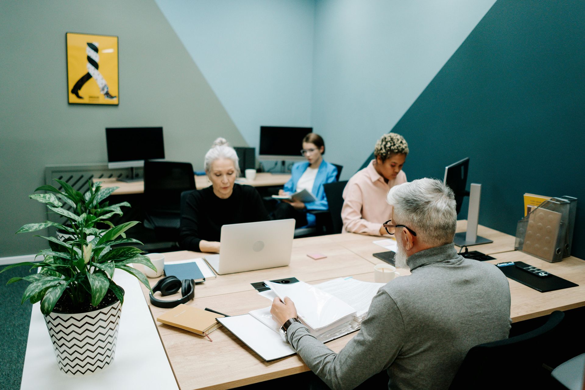 A group of people are sitting at a table with laptops in an office.