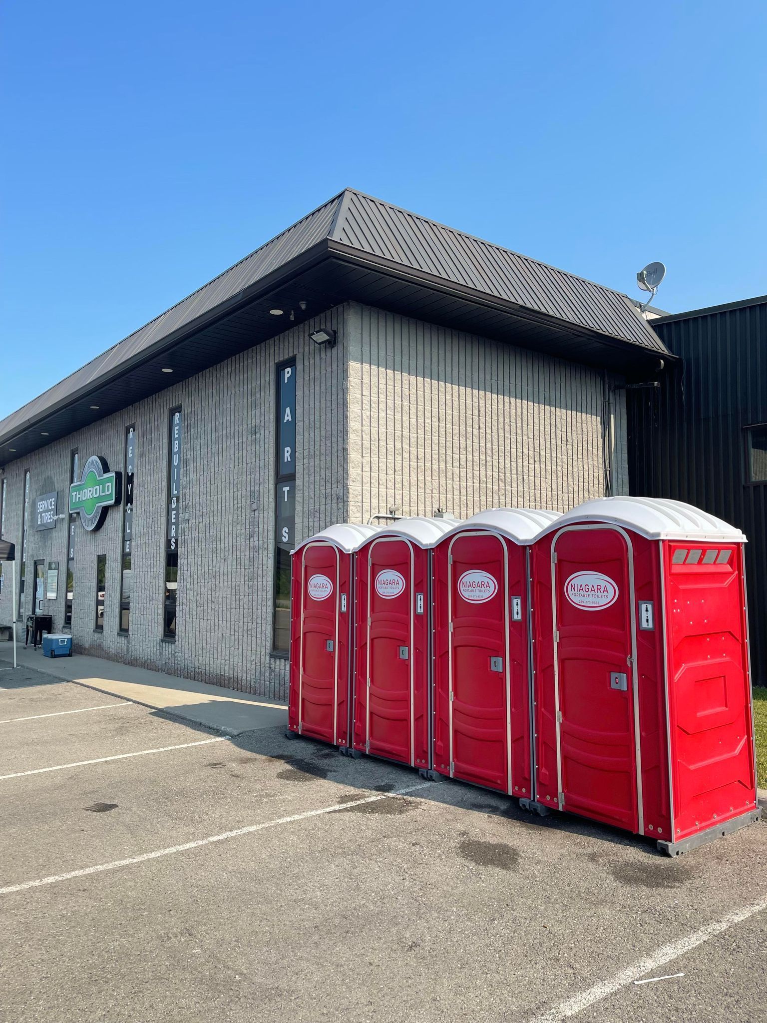 Four red portable toilets from Niagara Portable Toilets lined up outside a commercial building