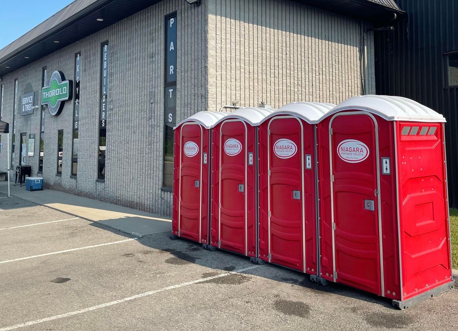 A row of red portable toilets are lined up in front of a building.