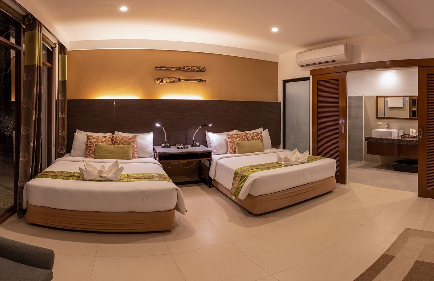 Hotel room with two beds, open door to bathroom, neutral tones.