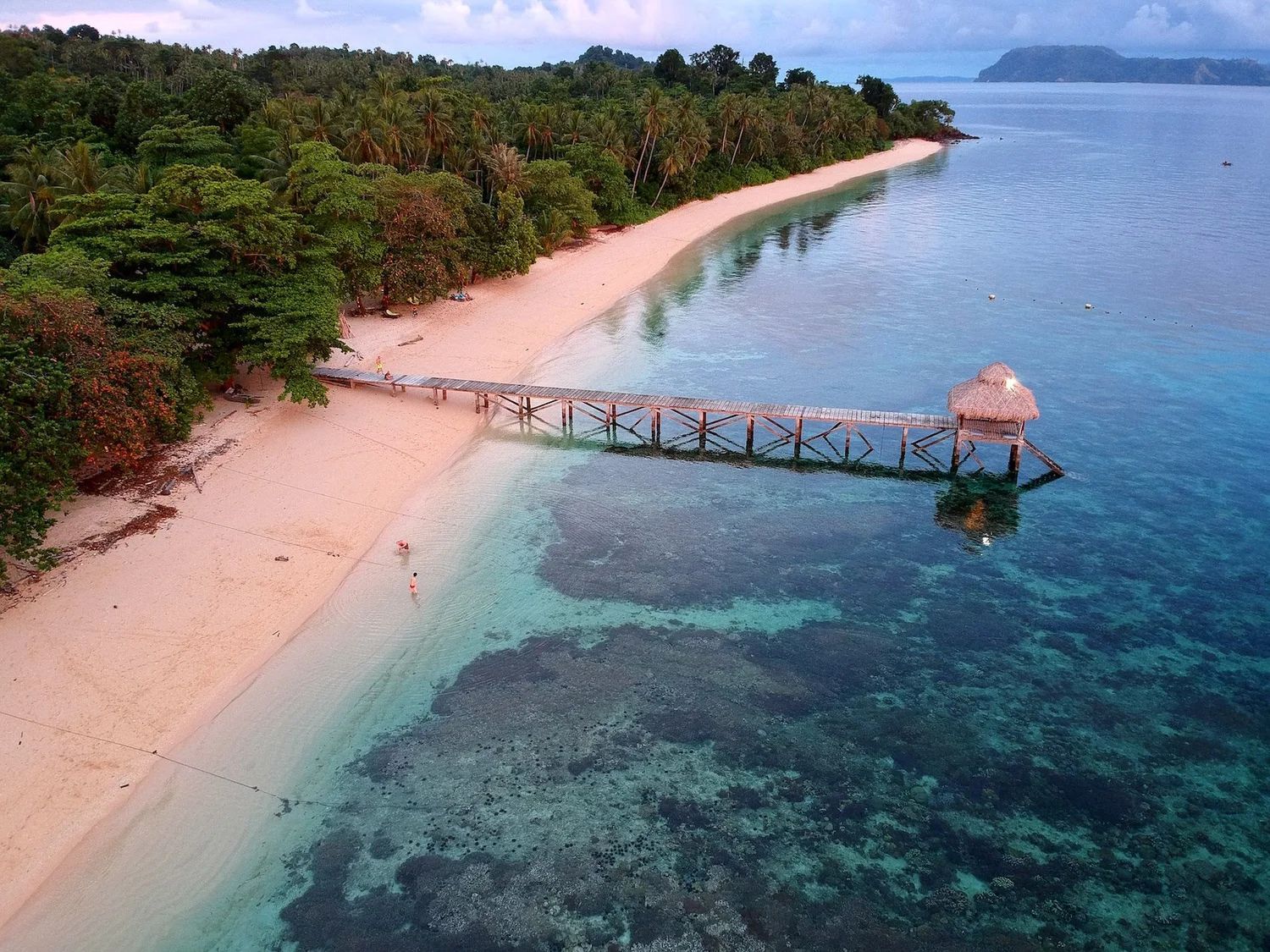 Bedroom with wooden furniture, four-poster bed with mosquito net, straw roof and woven walls.
