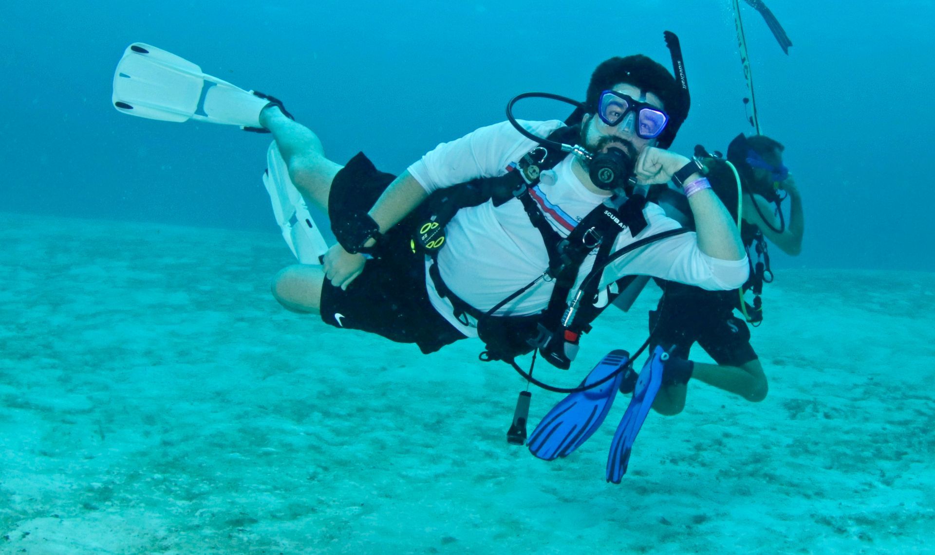 Person in scuba gear in water, smiling, trees and rocks in background.
