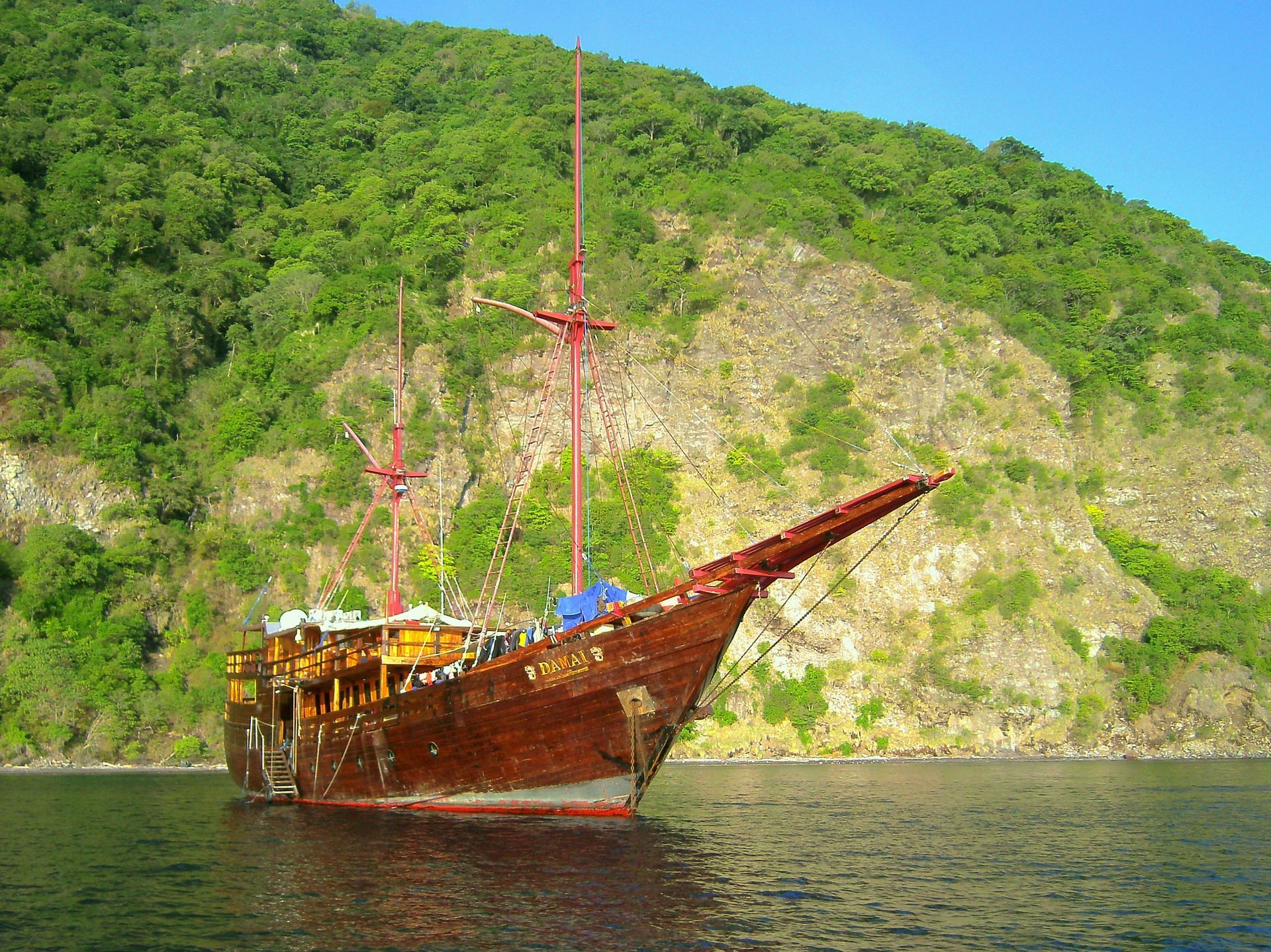 Wooden ship on water near a green, mountainous island.