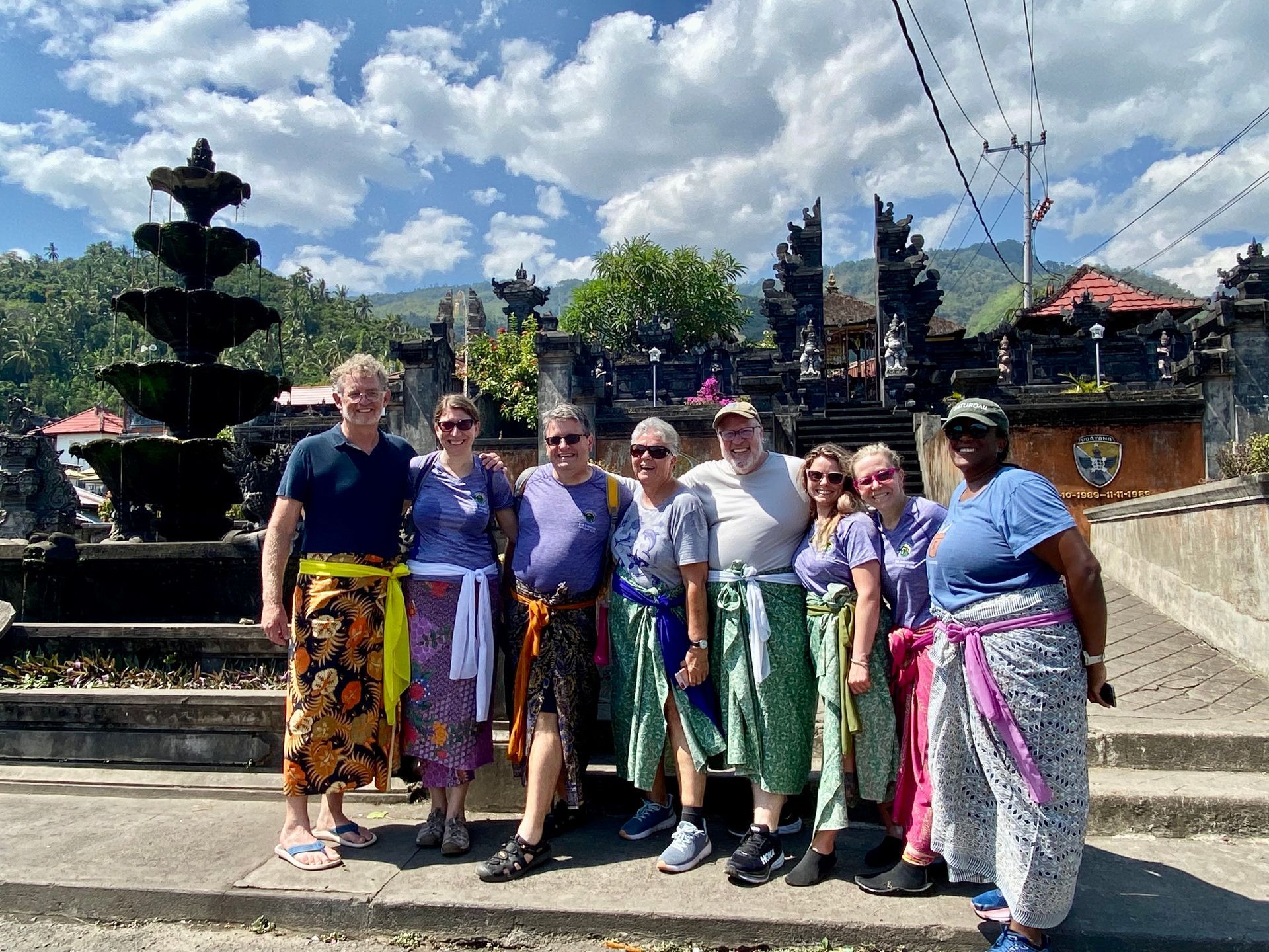 Group of people wearing sarongs poses in front of a Balinese temple with a fountain.