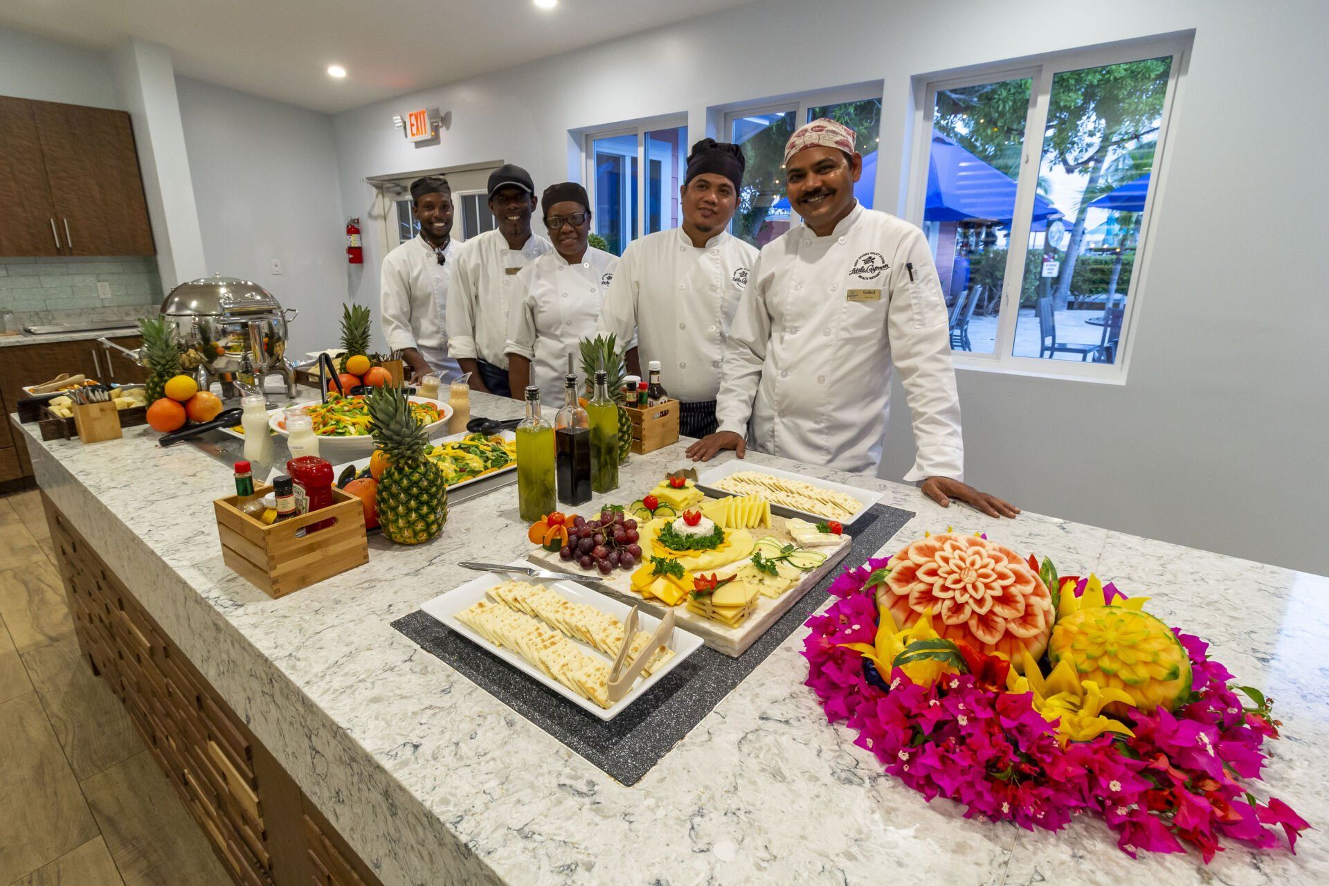 Chefs at a buffet counter with food and decor in a bright room.