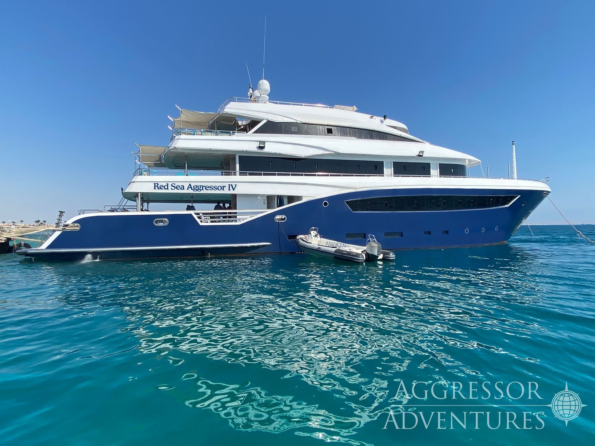 Blue and white Aggressor Adventures yacht in turquoise water.