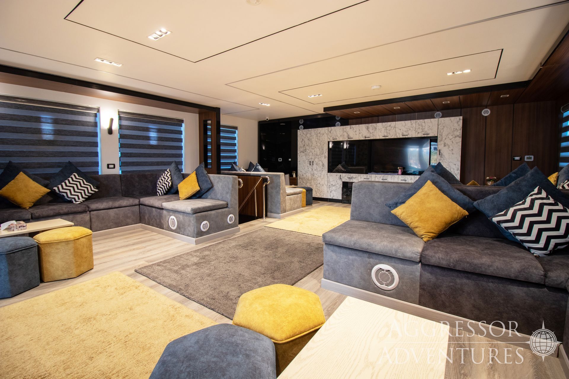 Living room with gray sofas, yellow pillows, patterned rugs, and television.