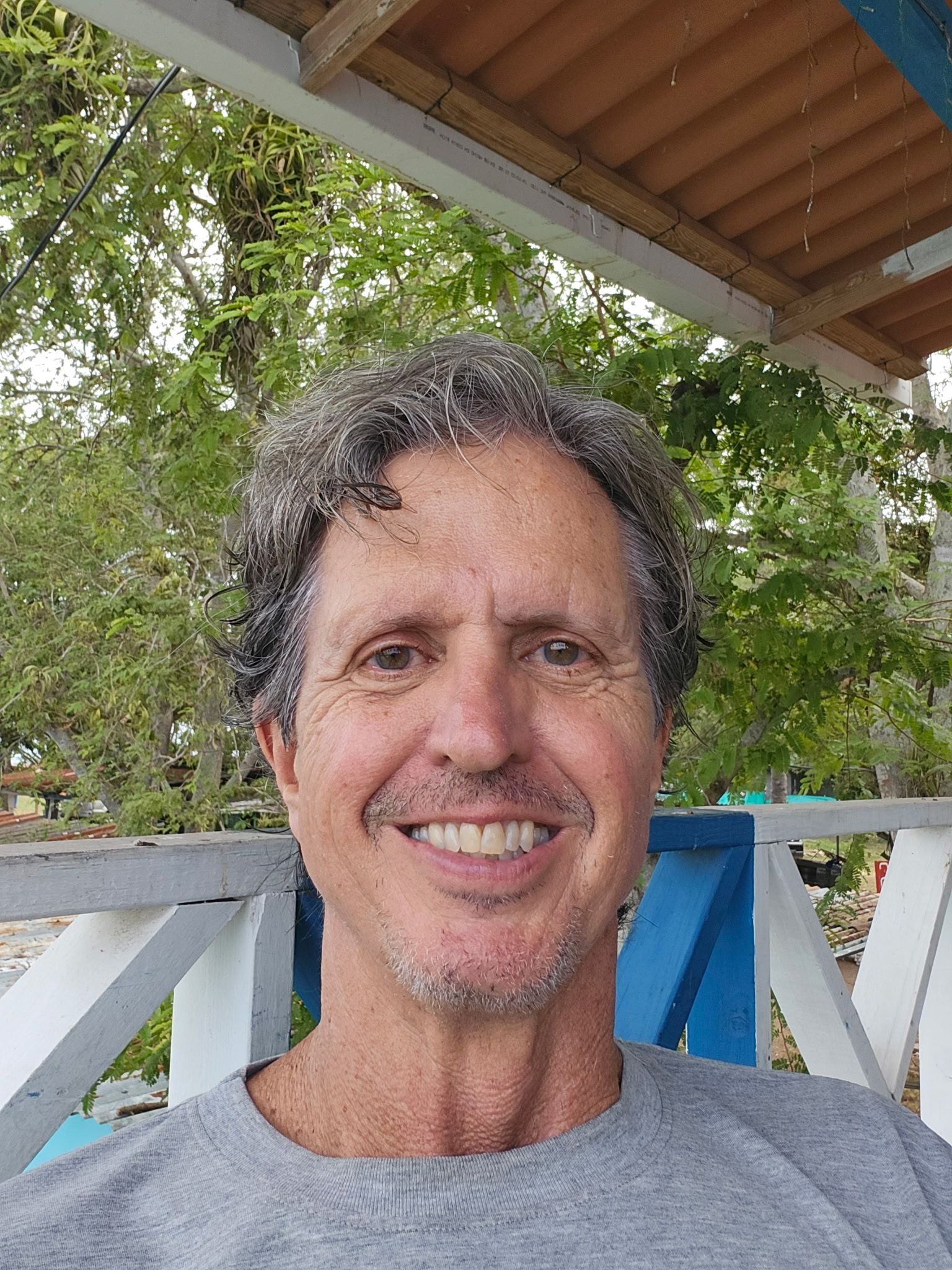Man wearing a black hat with a white brim and glasses smiling outside.