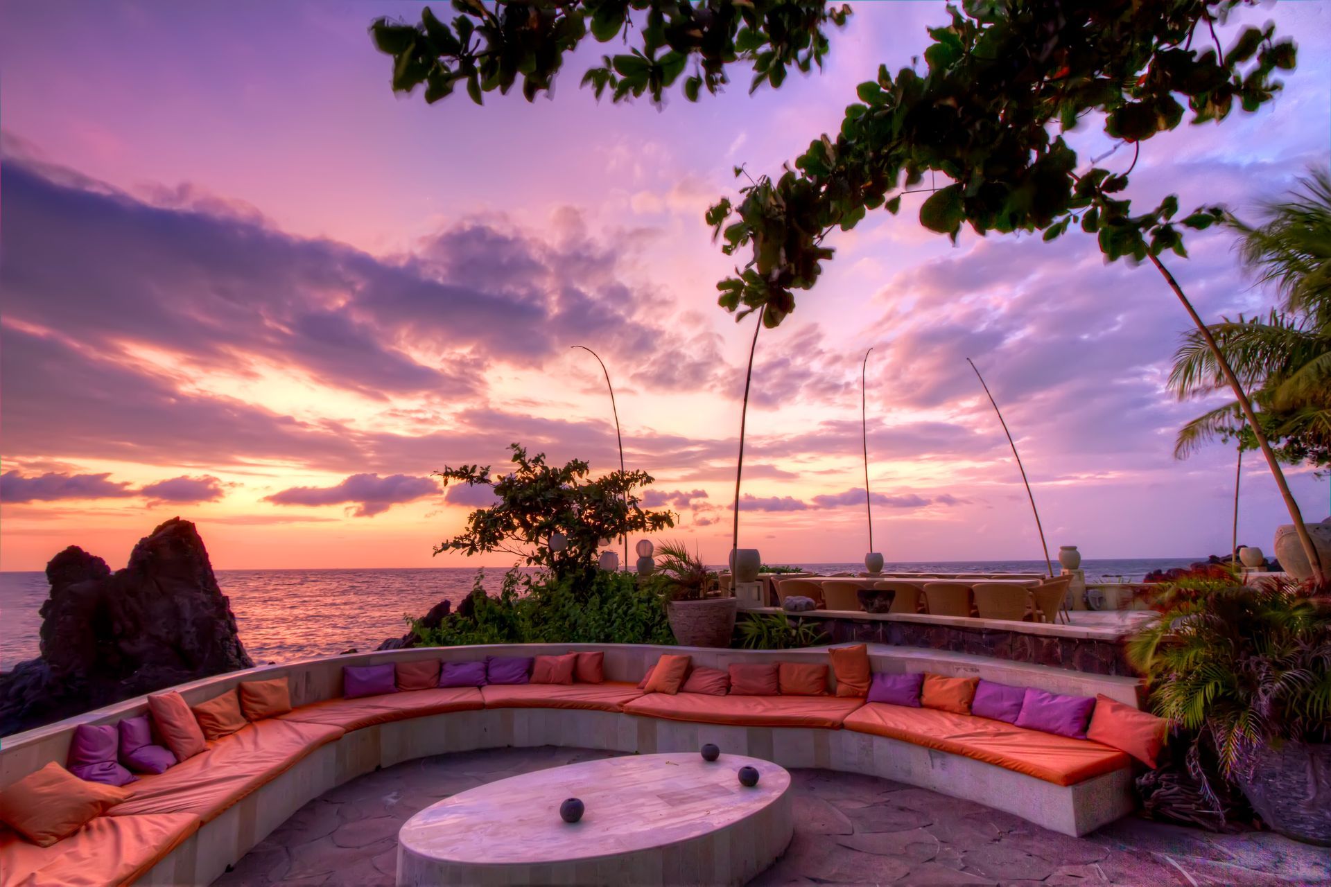 Curved outdoor seating with colorful cushions overlooking a sunset ocean view, Bali.
