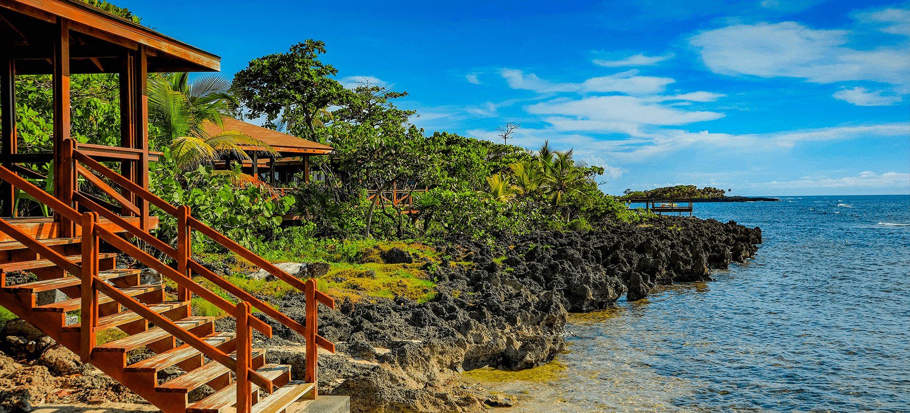 Wooden stairs leading to a gazebo on a rocky coast overlooking a blue ocean. Sunny day.