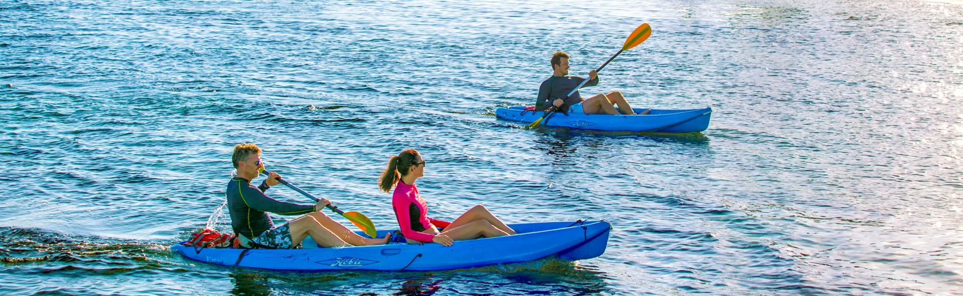 Two kayaks on a blue lake. Two people paddle in the first kayak, one in the second.