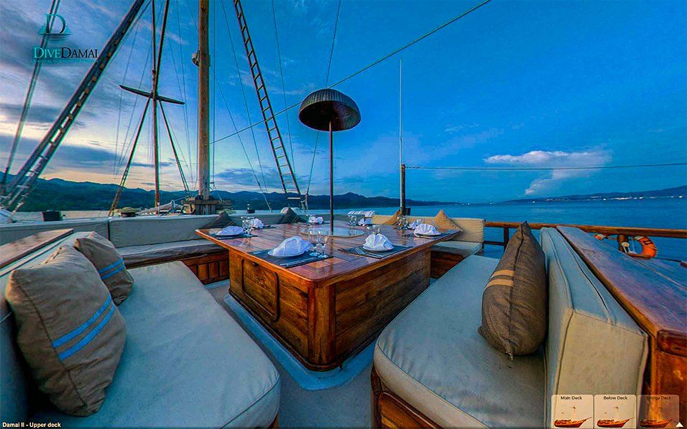 Wooden yacht deck at dusk, with dining table and seating, overlooking the sea.