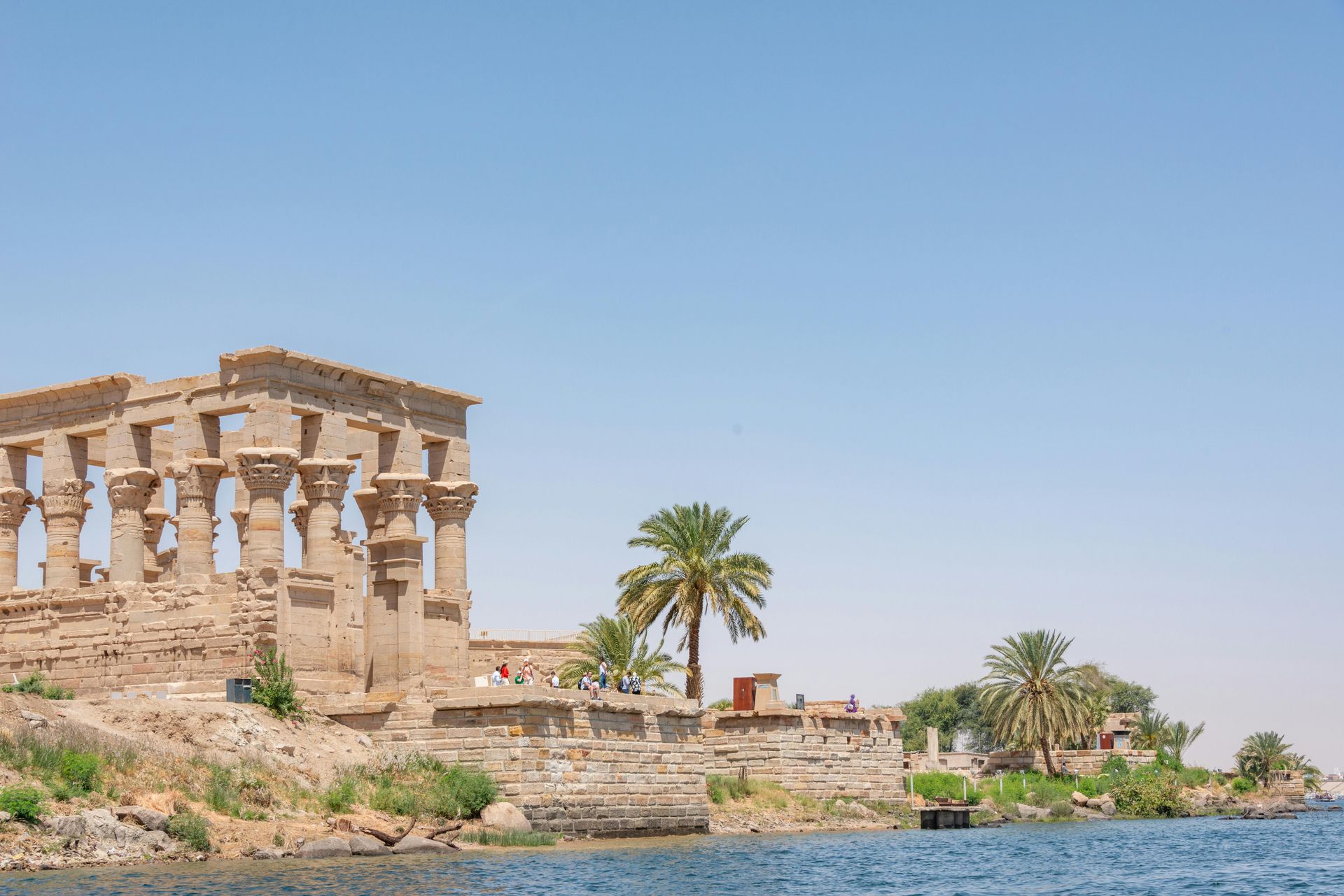 Ancient Egyptian temple ruins on a shoreline, blue sky overhead.