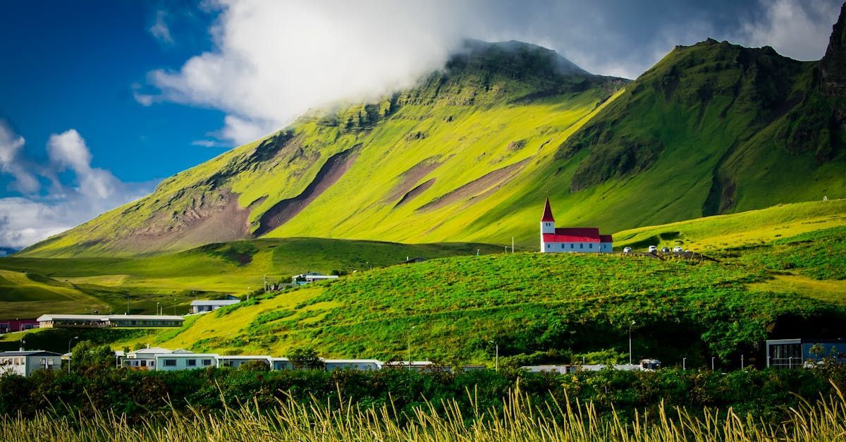 Green hills with a white church, red steeple, and village beneath a cloudy mountain.