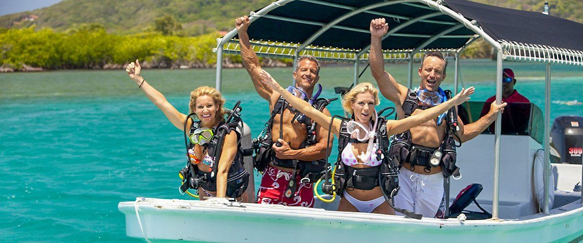 People in scuba gear celebrate on a boat in turquoise water.