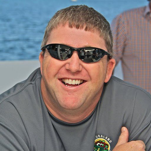 Man wearing sunglasses smiles broadly, outdoors.