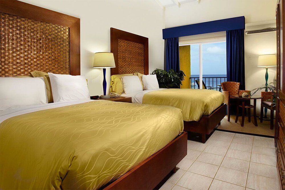 Two beds in a hotel room with woven headboards, overlooking a balcony and ocean.