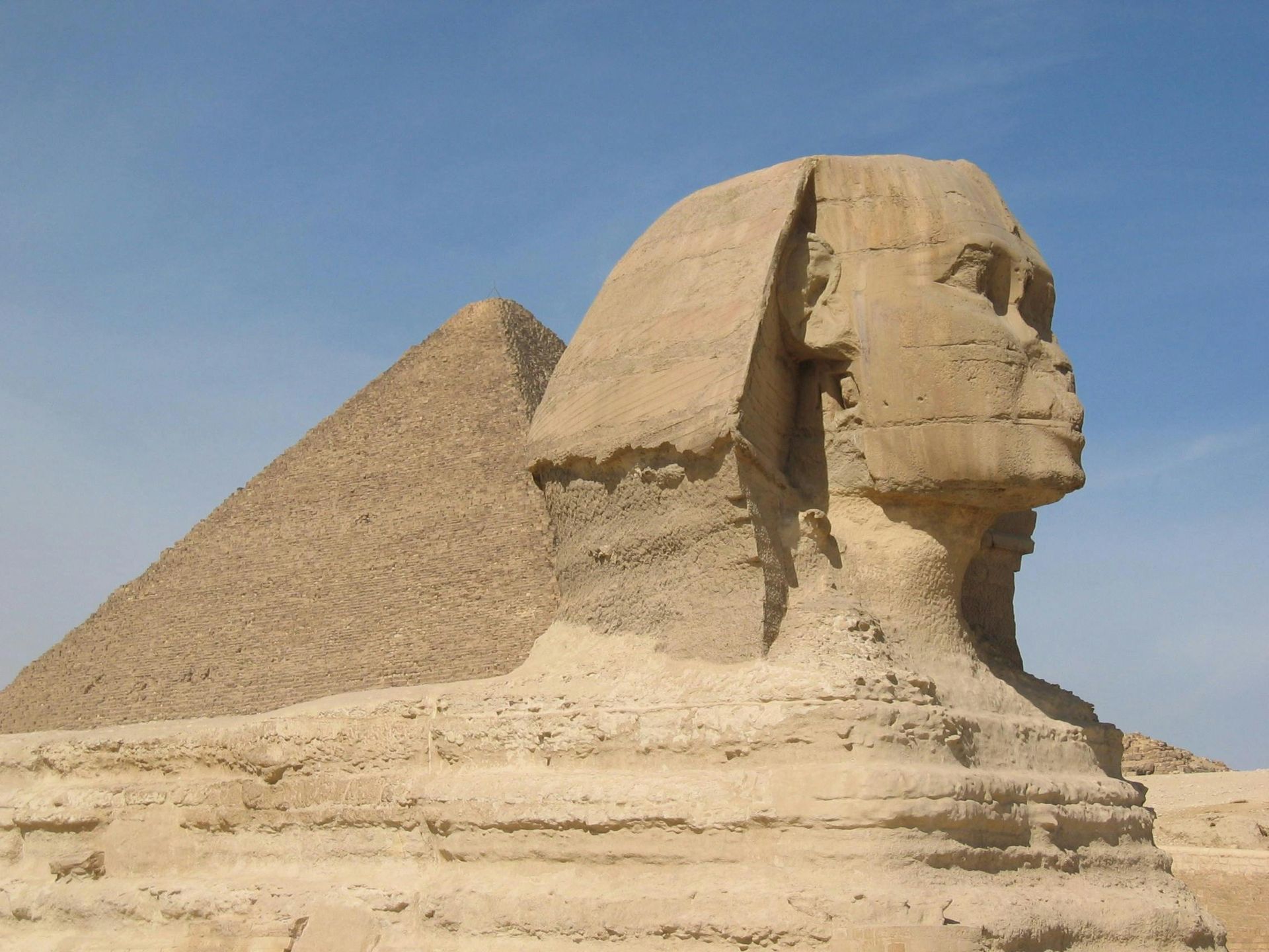 Great Sphinx of Giza, Egypt, with a pyramid in the background, set against a clear blue sky.