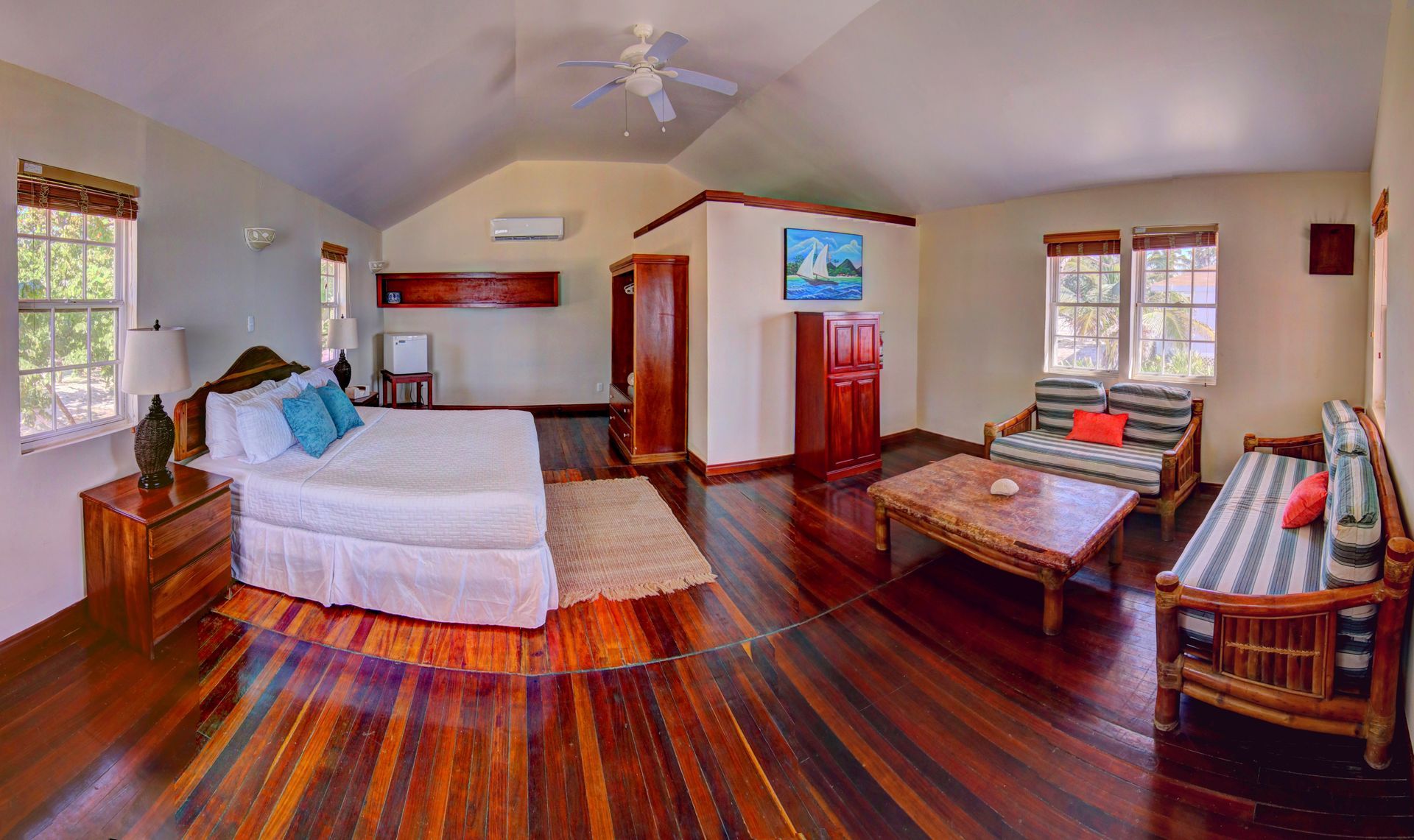 Spacious bedroom with hardwood floors, a king-size bed, seating area, and wooden furniture.