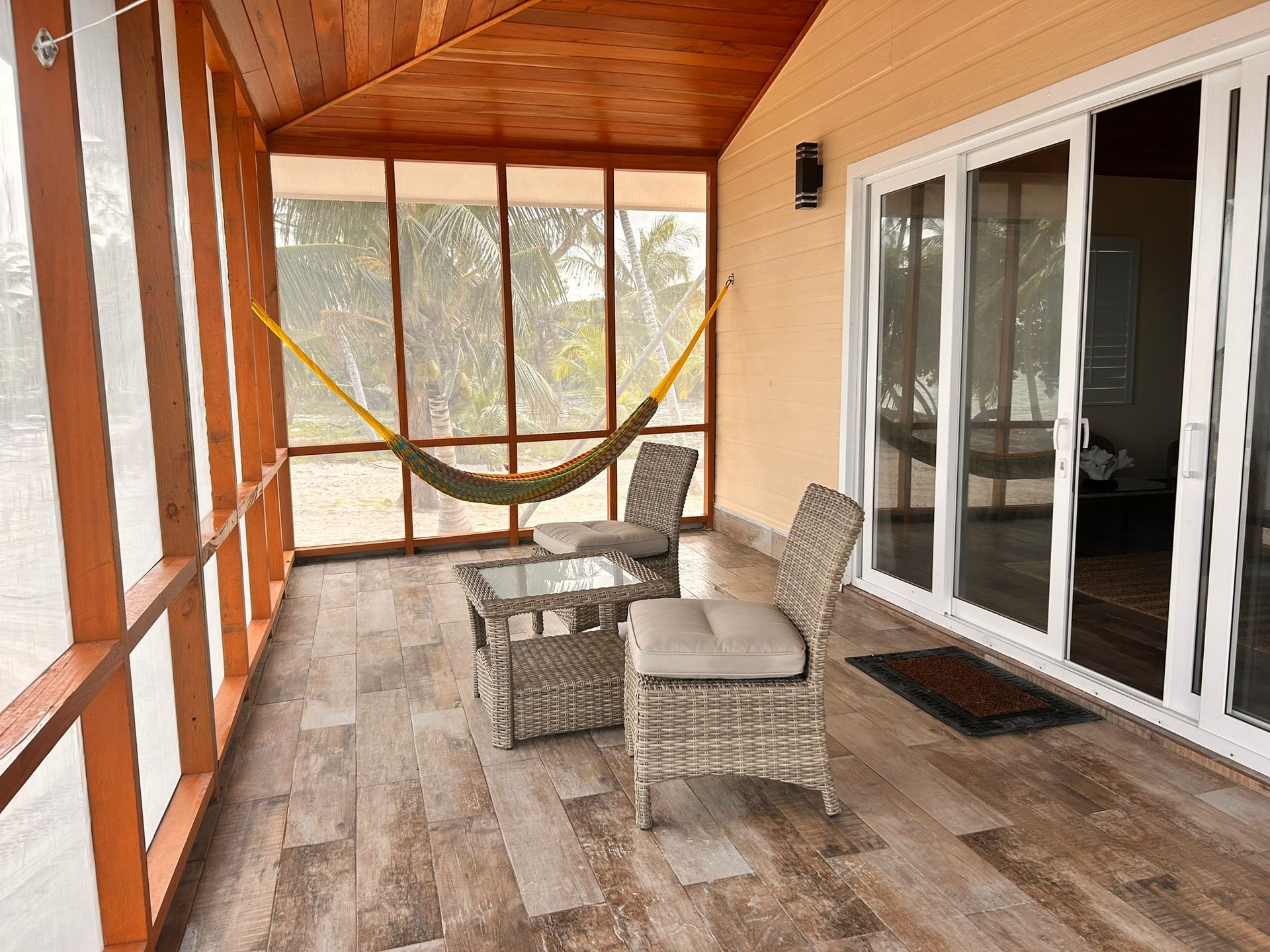 Screened porch with woven furniture, a hammock, and sliding glass doors.