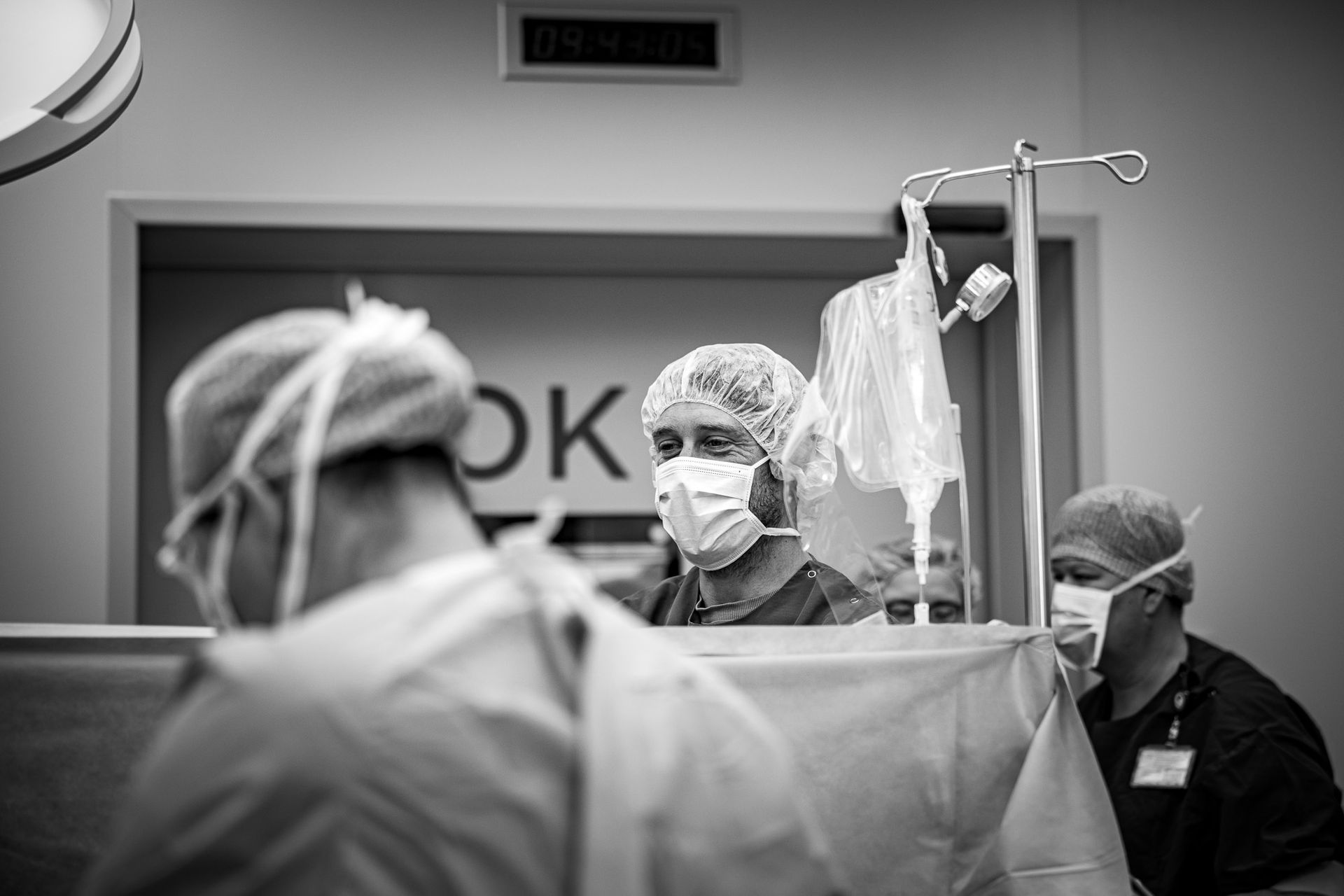 Vader kijkt ontroerd toe tijdens keizersnede in het ziekenhuis, vastgelegd door geboortefotograaf in Overijssel.