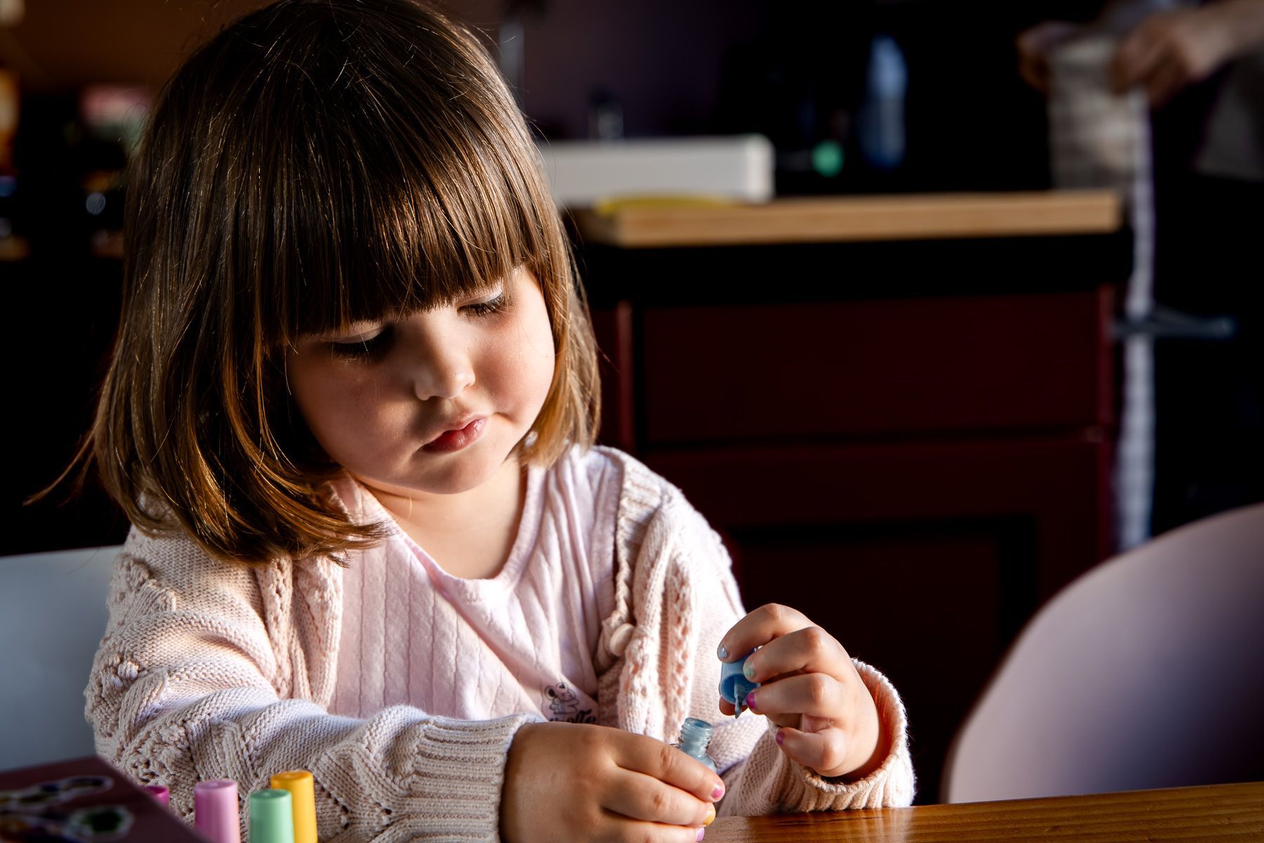 Peuter speelt geconcentreerd met nagellak aan tafel.