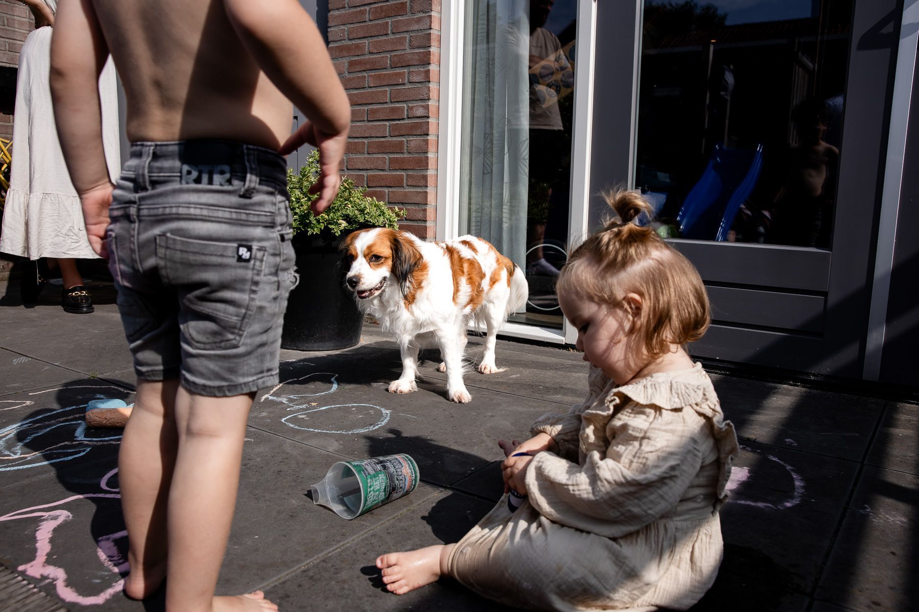 Twee jonge kinderen spelen buiten met stoepkrijt op het terras, met de hond erbij