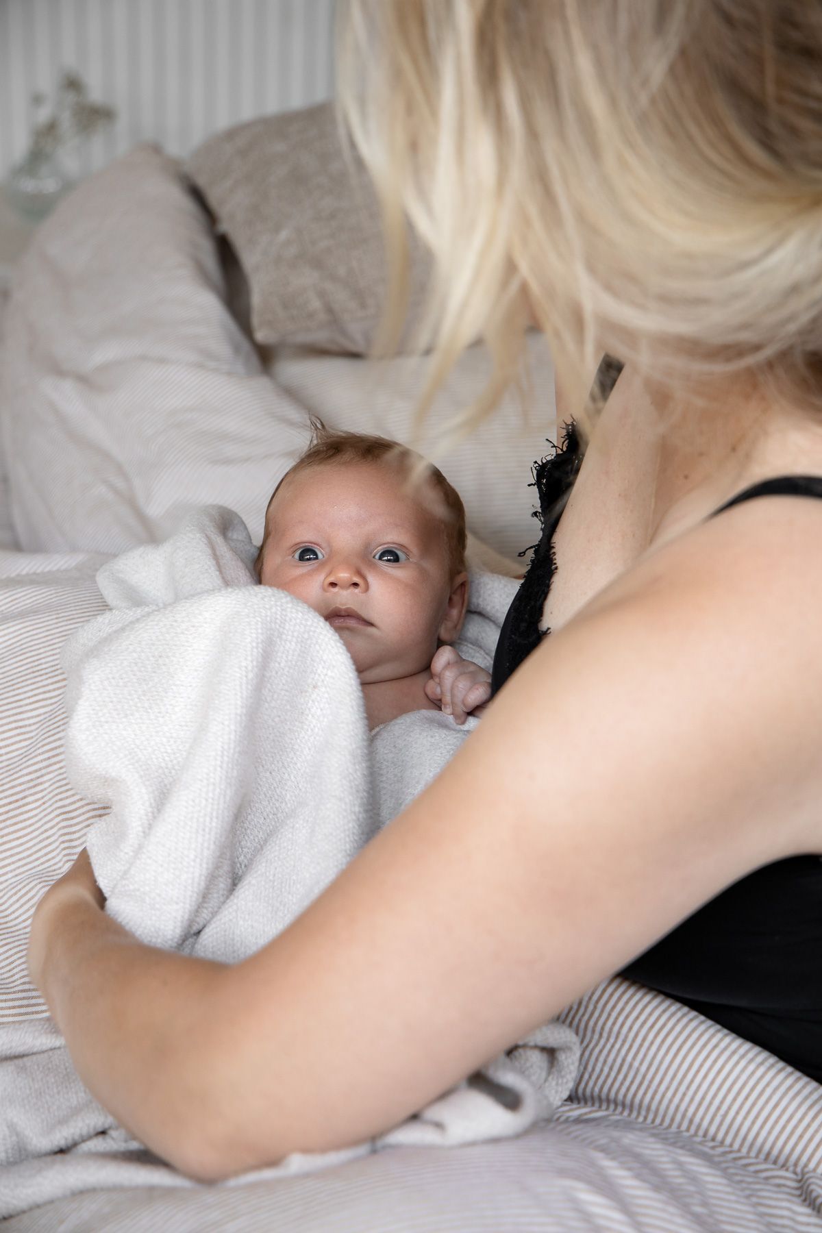 Pasgeboren baby ligt op bed bij moeder en kijkt met open ogen