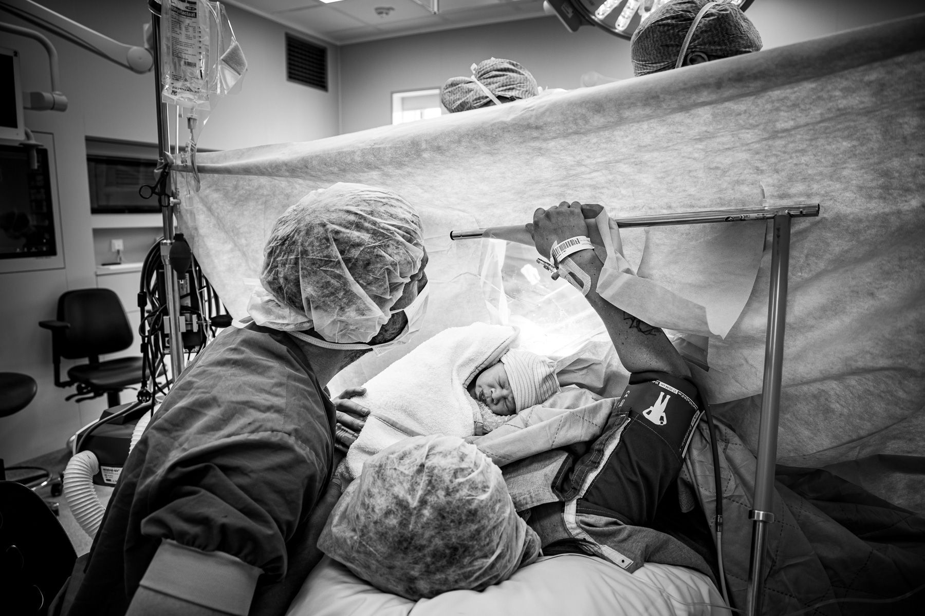 Pasgeboren baby direct na een keizersnede op de borst van de moeder in de operatiekamer, terwijl vader meekijkt met ingreep