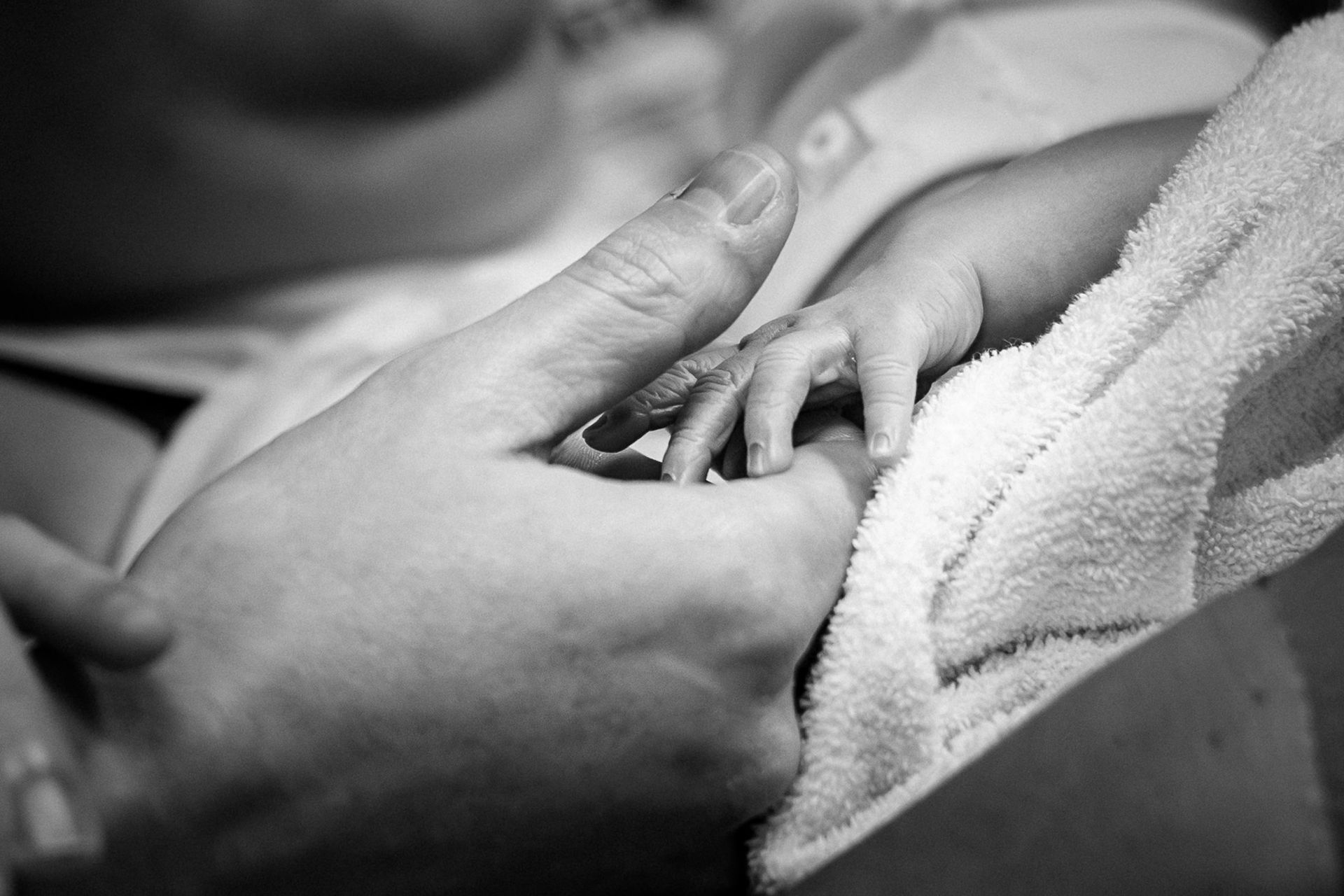 Detail van een babyhandje dat de hand van een ouder vasthoudt