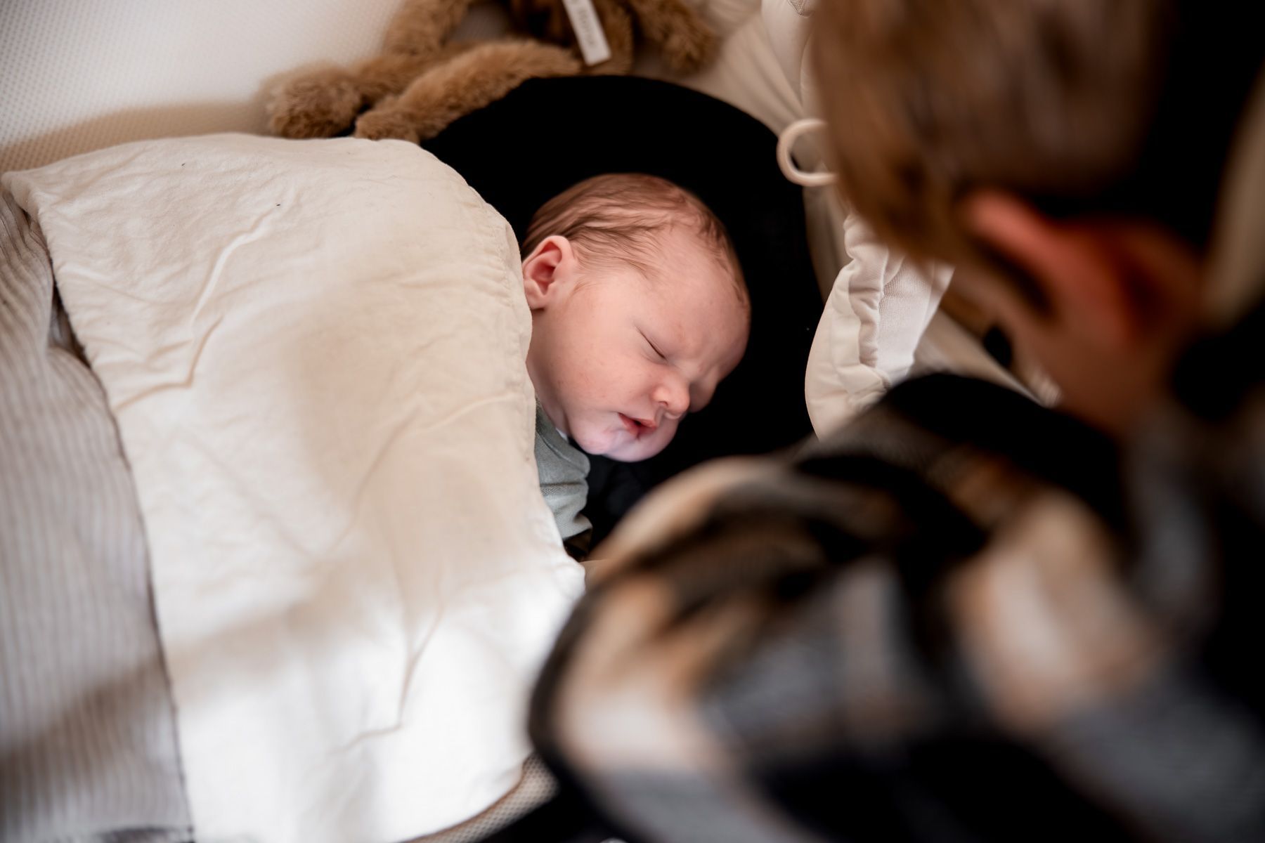 Slapende pasgeboren baby ligt onder een dekentje terwijl grote broer toekijkt.