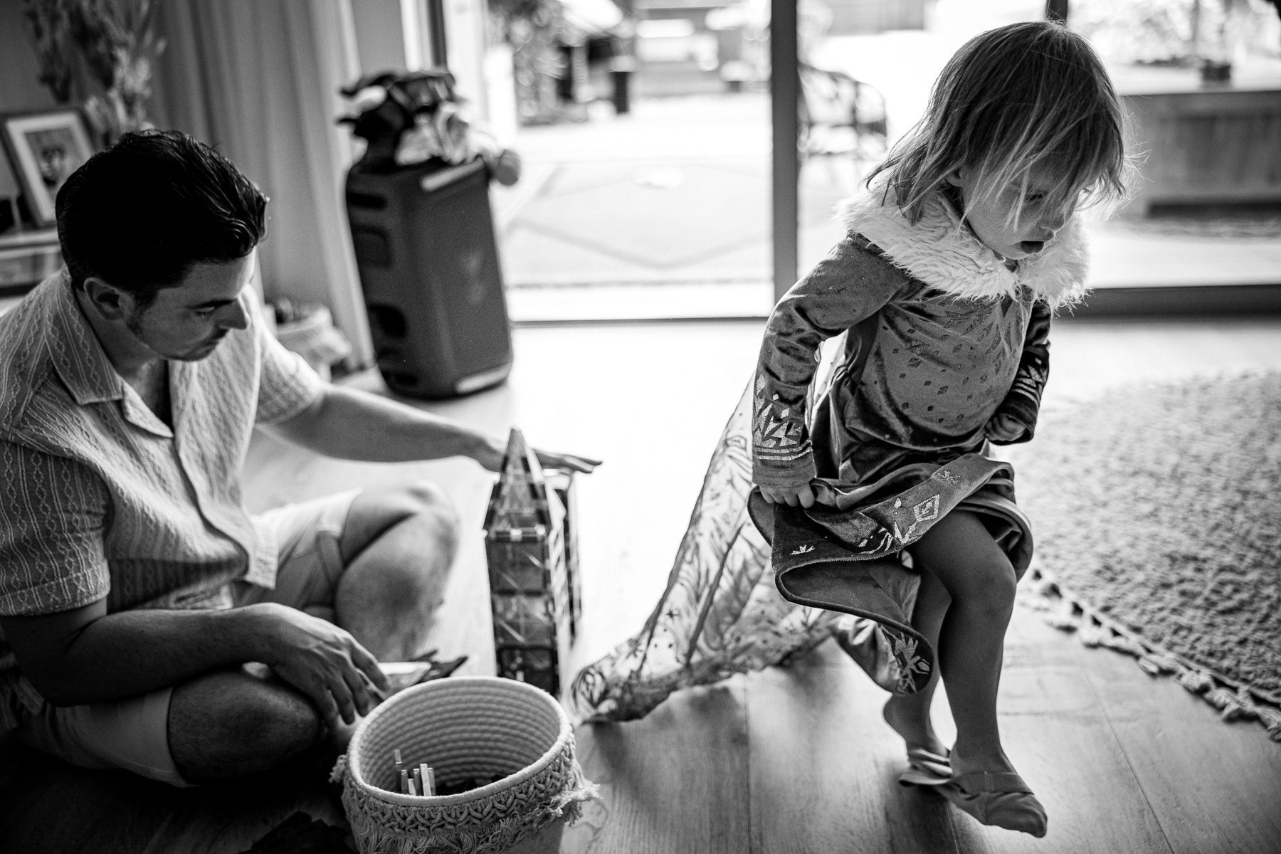 Vader zit op de grond terwijl een kind spelend door de woonkamer loopt.