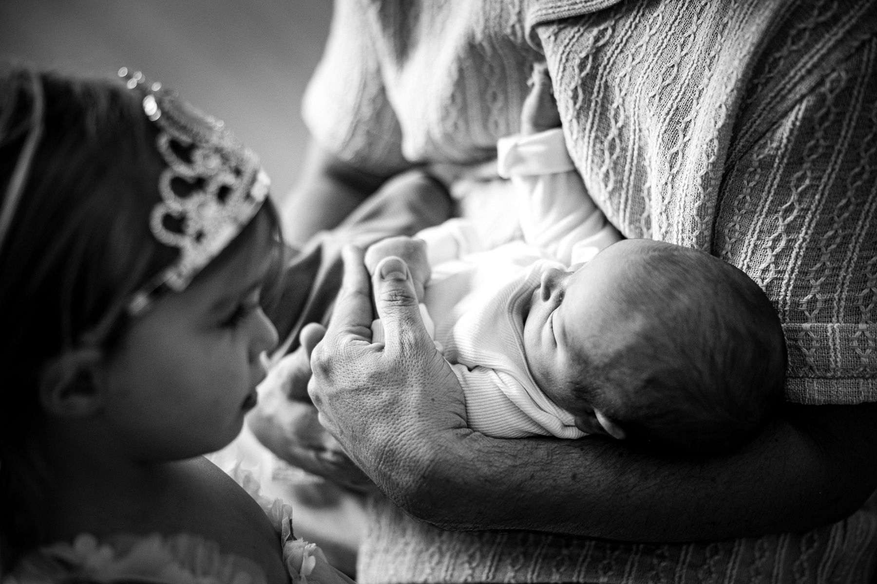 Oudere zus kijkt naar haar pasgeboren babybroertje dat in armen wordt vastgehouden.