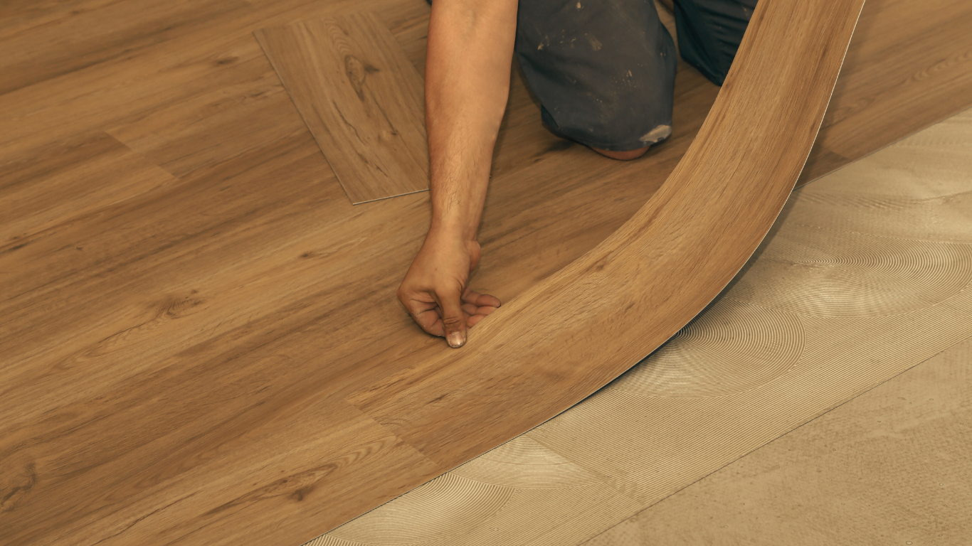 Person installing vinyl flooring, rolling out a section onto a beige underlayment.