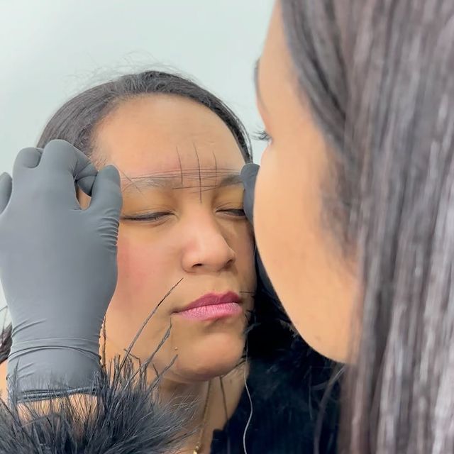 A woman is measuring her eyebrows in front of a mirror.