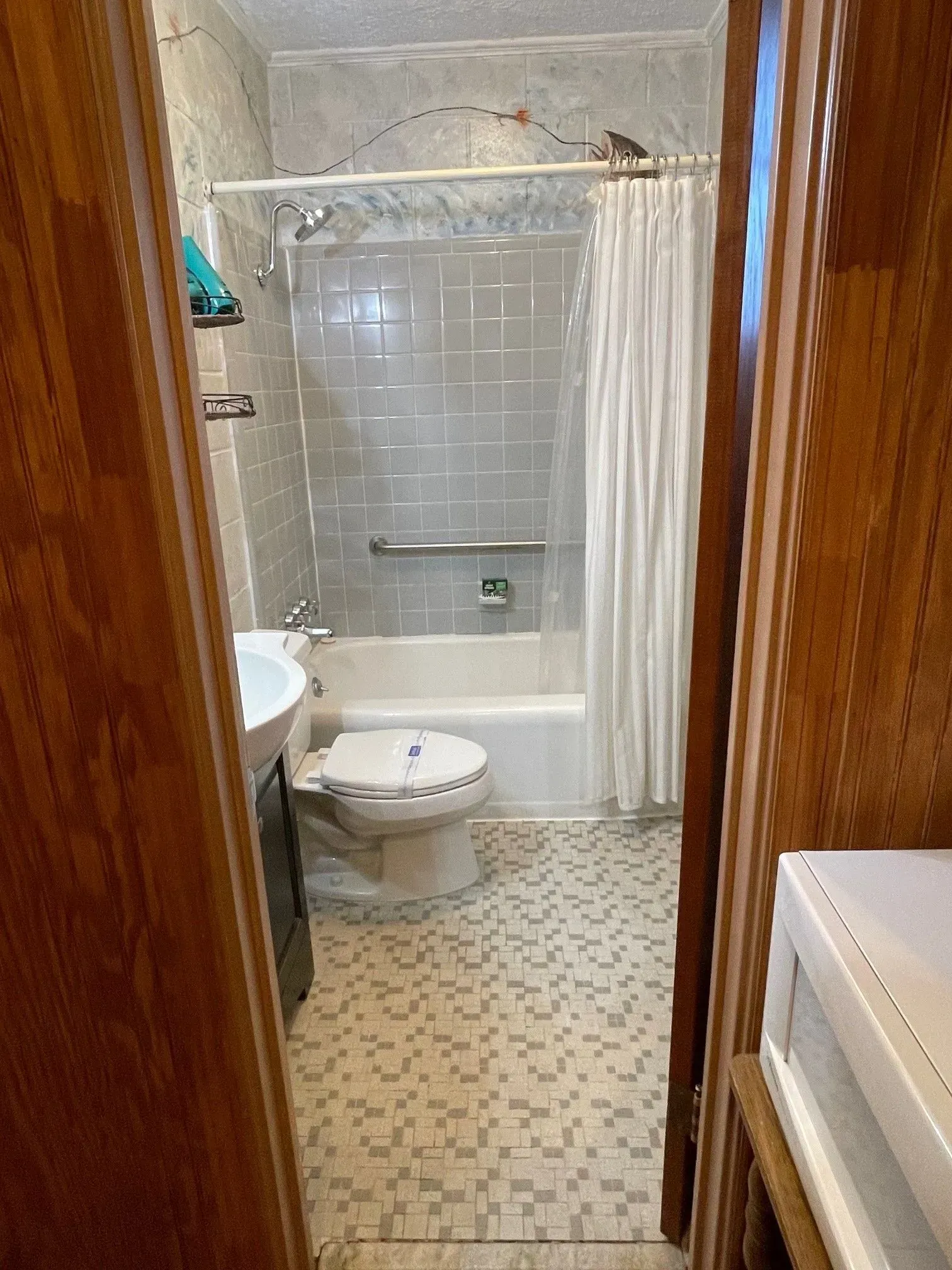 Bathroom viewed from doorway with toilet, tub, and shower. Features tile floors and walls with white shower curtain.