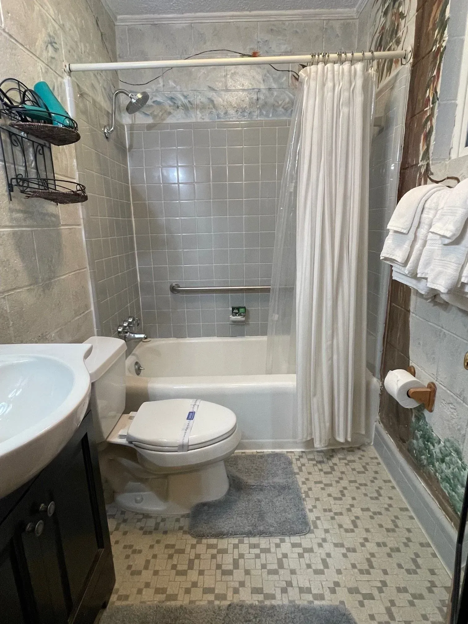 Bathroom with tub, shower, toilet, and vanity. Gray tiled walls and floor. White shower curtain.