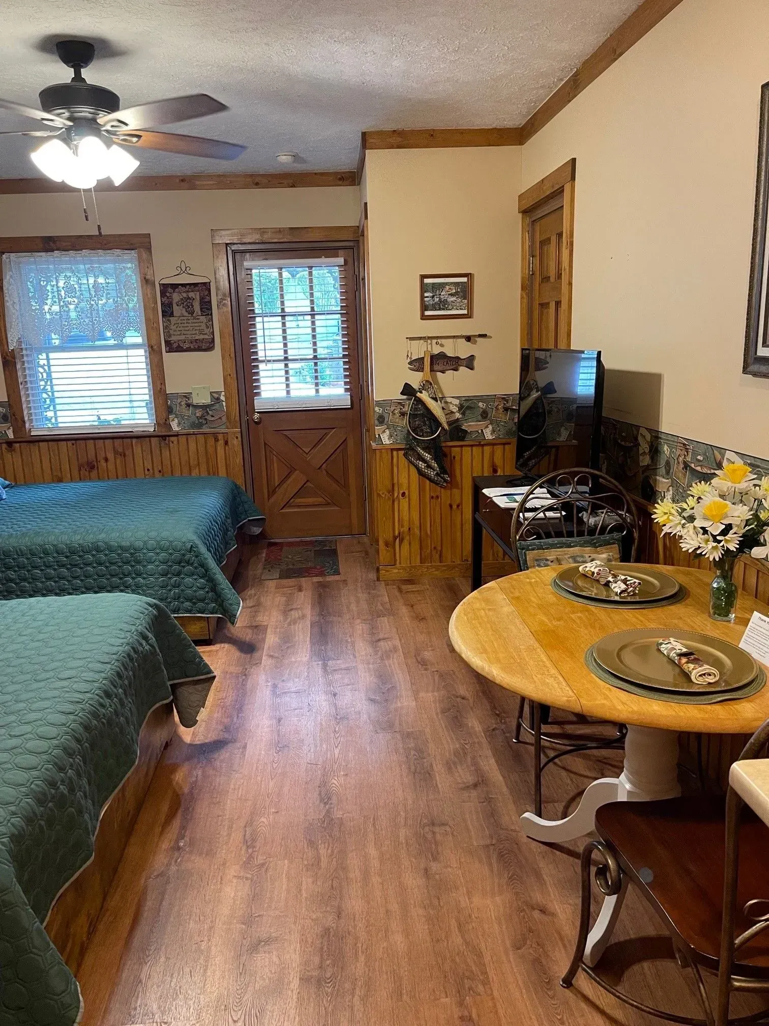 Cozy cabin room with three beds, round table, TV, and a wooden door.