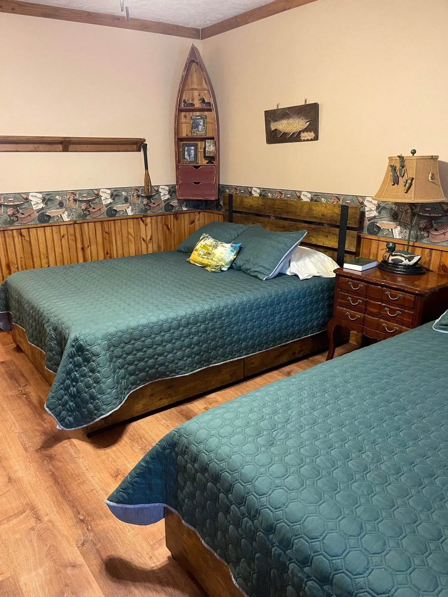 Two beds with green quilts in a wood-paneled room with fishing decor.