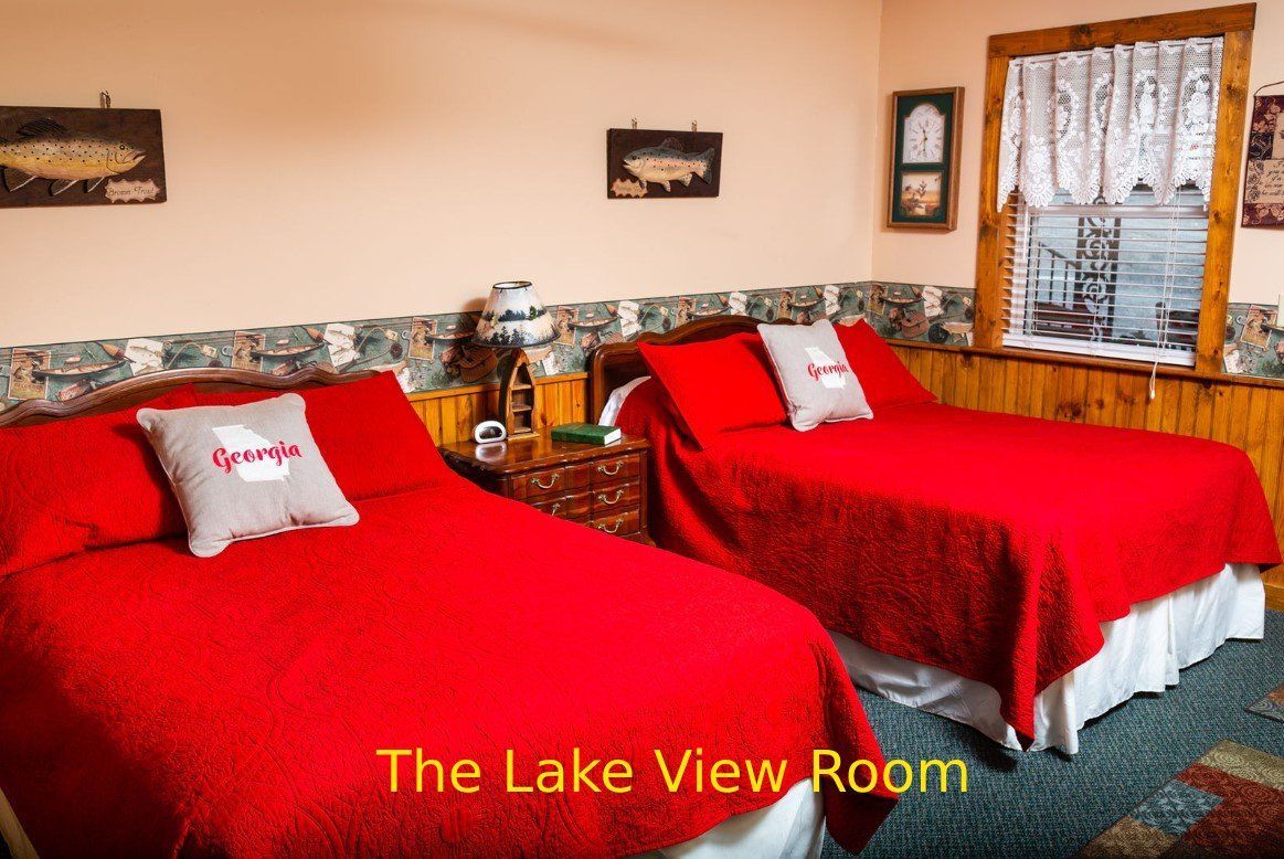 A hotel room with two red beds, a window, and wall decorations. The room is