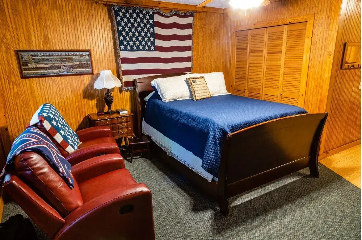 Bedroom with American flag, wooden walls, blue bedspread, red recliner.