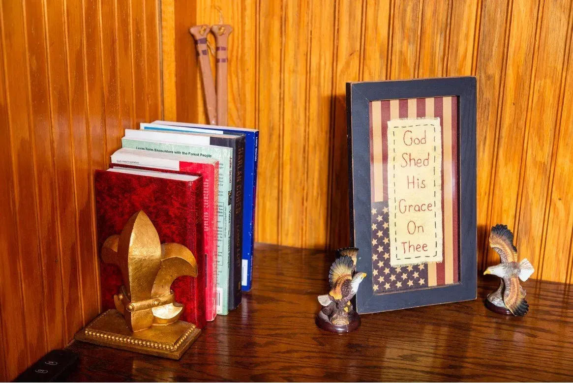 Books with a fleur-de-lis bookend, framed patriotic quote, and decorative figurines on a wooden surface.