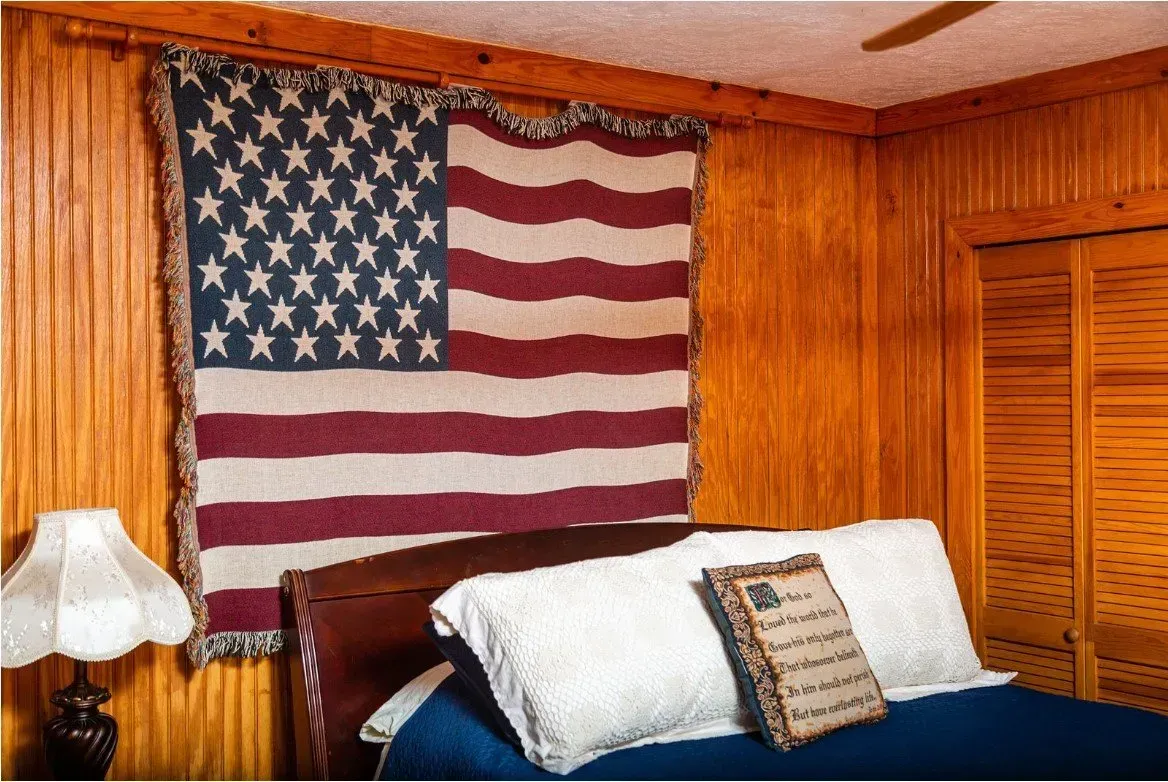 Bedroom with American flag tapestry above the bed. Wooden paneling and shutters.