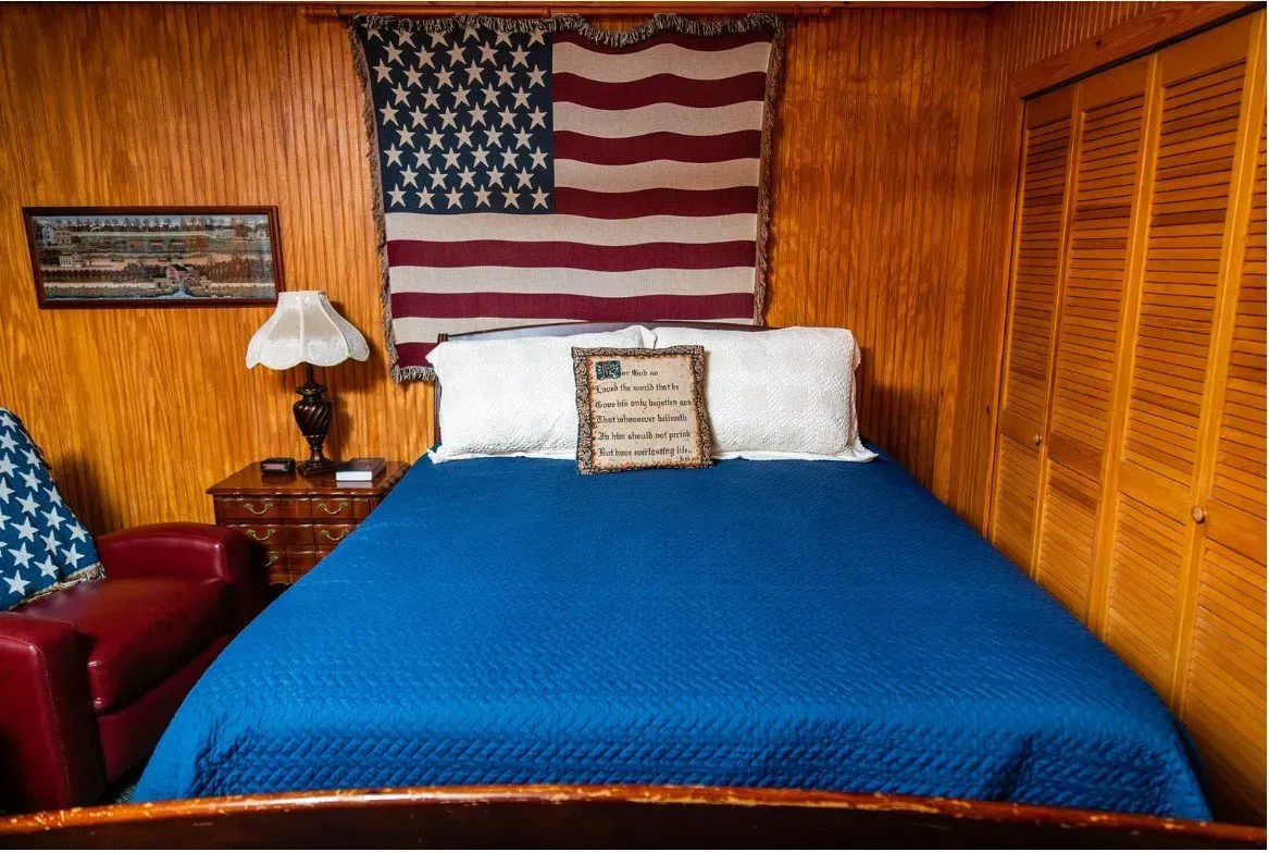 Bedroom with blue bedspread, American flag wall decor, wood paneling, red armchair.