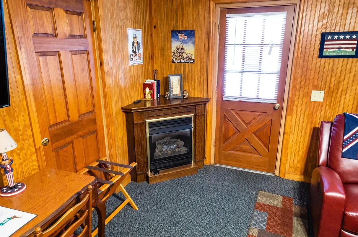 Cozy room with wooden paneling, a corner fireplace, desk, door, and red recliner. Americana decor.