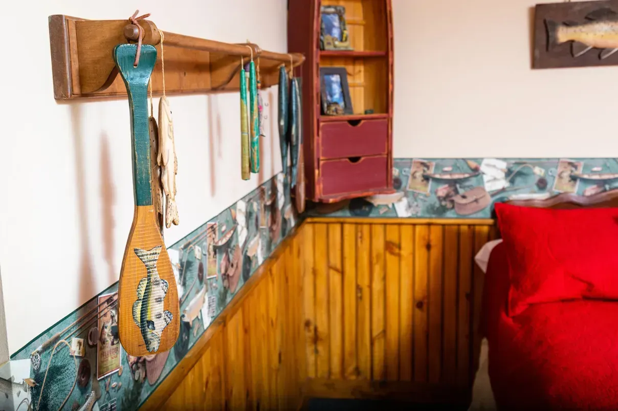 Wooden decorative paddles hang on a wall with fish wallpaper, next to a red bed.