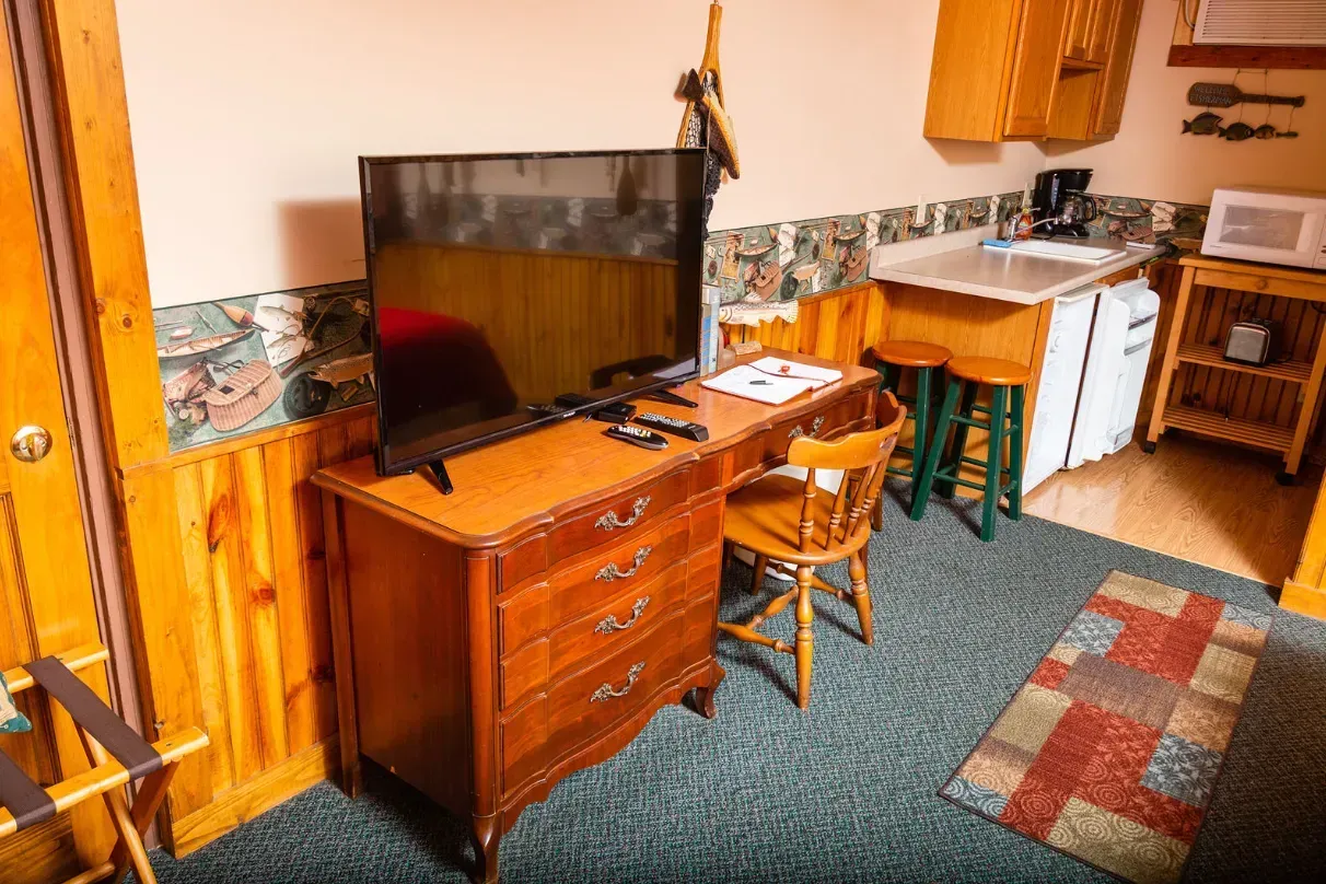 A small rustic cabin room with a TV, desk, and kitchenette.